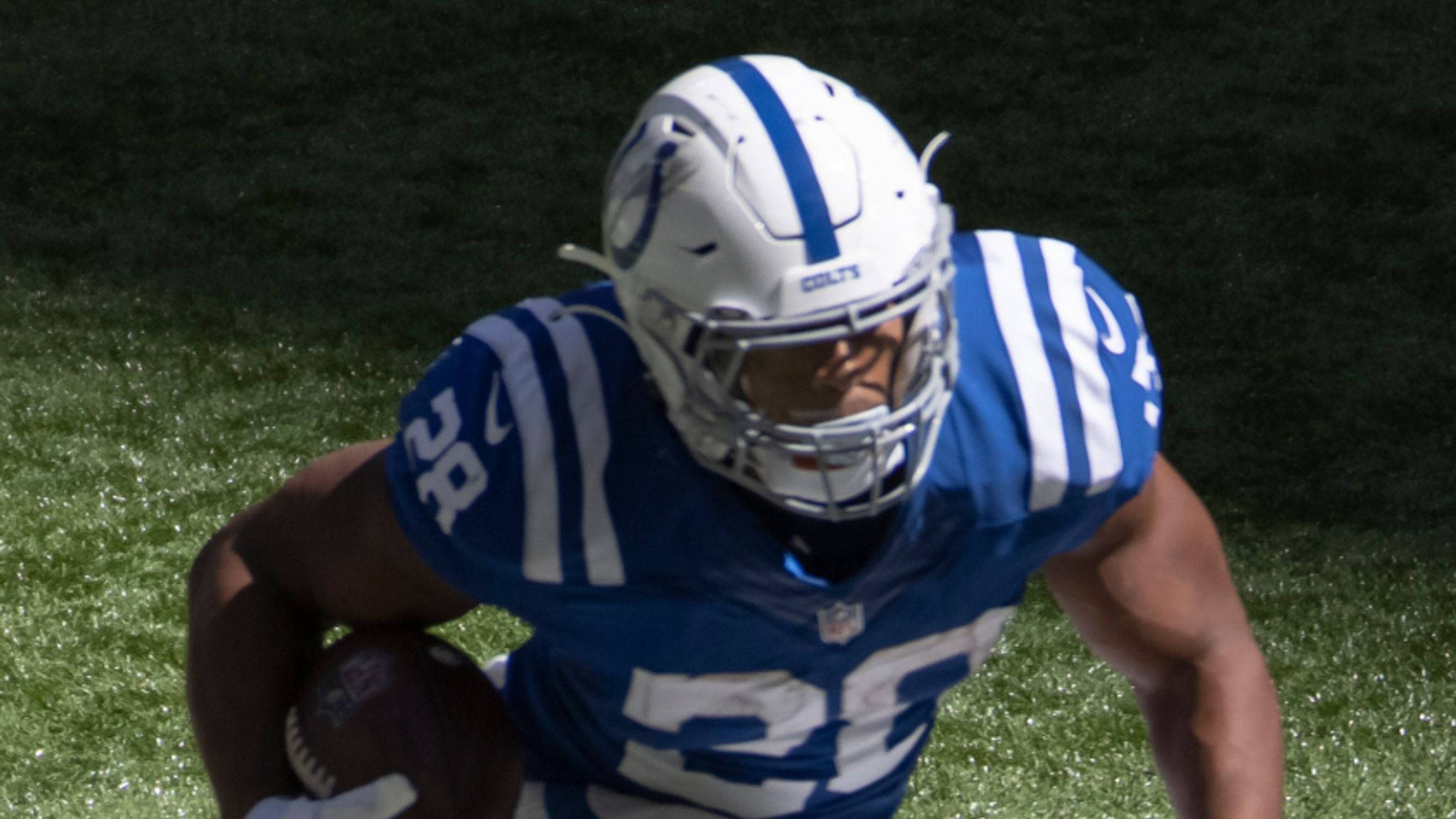 Jonathan 桌布 壁紙 — 一名身穿藍白 Colts 裝備的美式足球員在陽光明媚的綠色球場上持球衝刺。