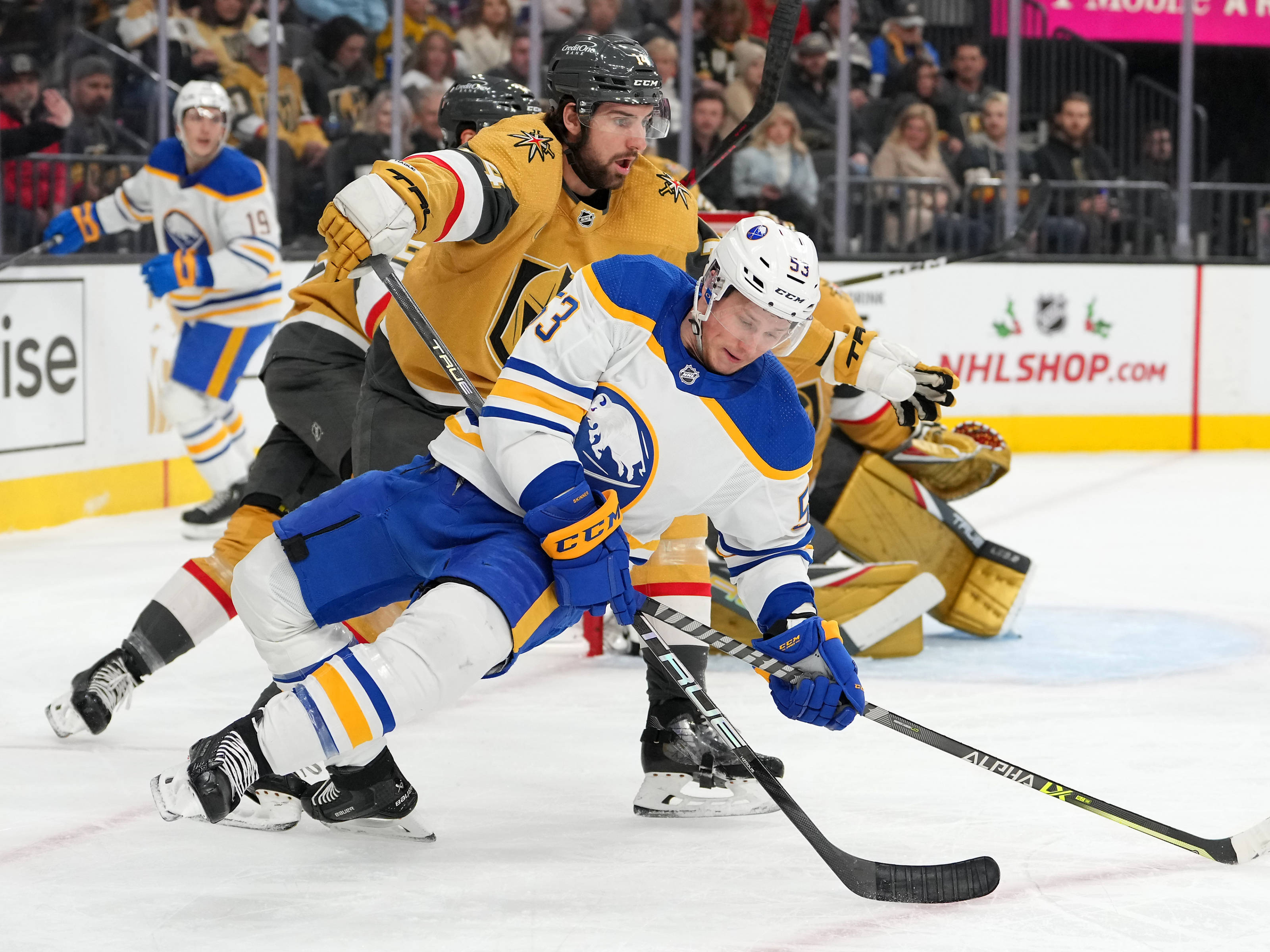 hockey 桌布 壁紙 — 一名身穿藍白色球衣的冰球運動員在冰上低身滑行，爭奪控球權，而身穿金色球衣的對手在緊張的比賽中施壓。