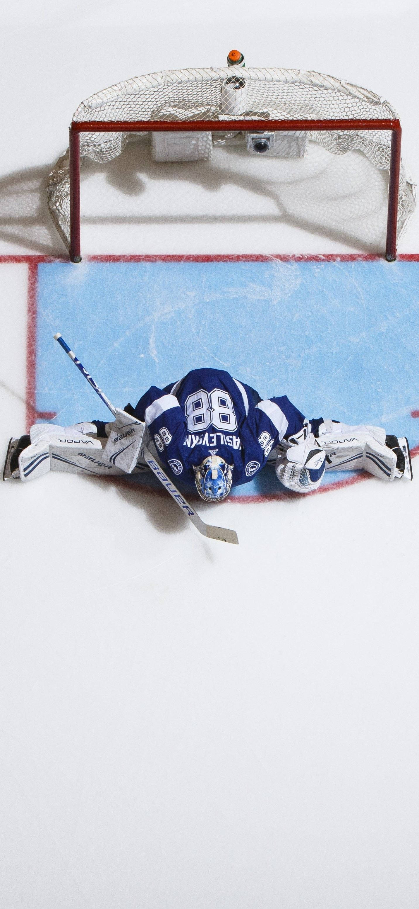 Tampa Bay Lightning 桌布 壁紙 — 一名身穿藍白色裝備的冰球守門員在冰場上飛撲，試圖擋下靠近球門的射門。