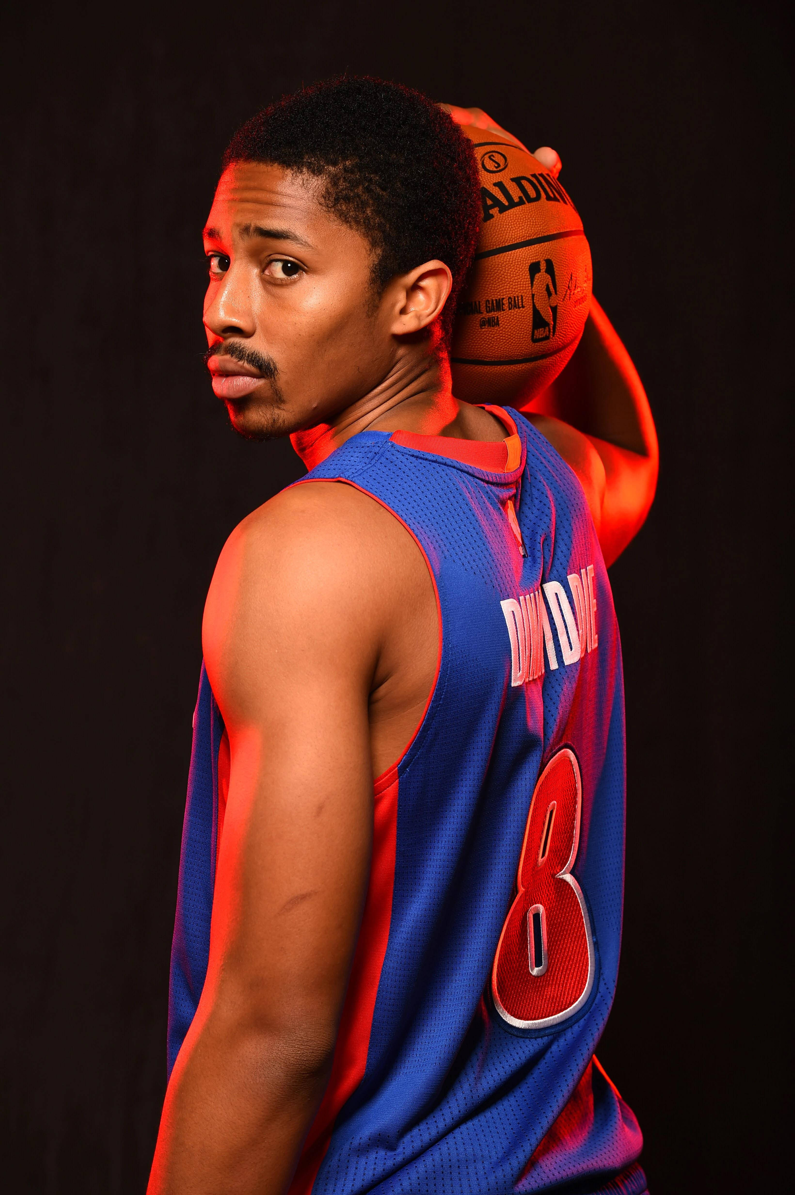 spencer dinwiddie 桌布 壁紙 — 一名身穿藍紅球衣的籃球運動員在黑暗背景和戲劇性的紅色燈光下，將球舉過肩膀。
