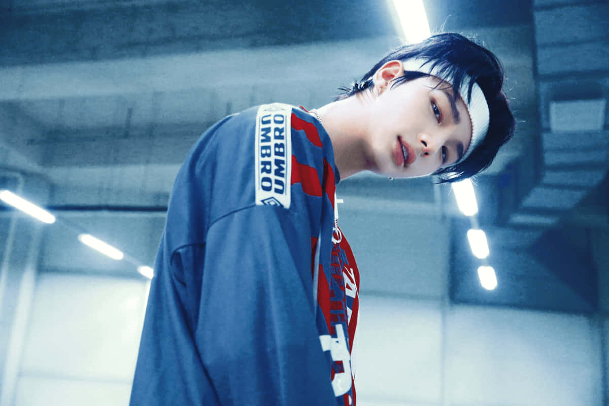 hyunjin 桌布 壁紙 — 一名身穿藍紅相間Umbro襯衫的年輕男子在冷色調工業空間的明亮頂燈下向前傾身。