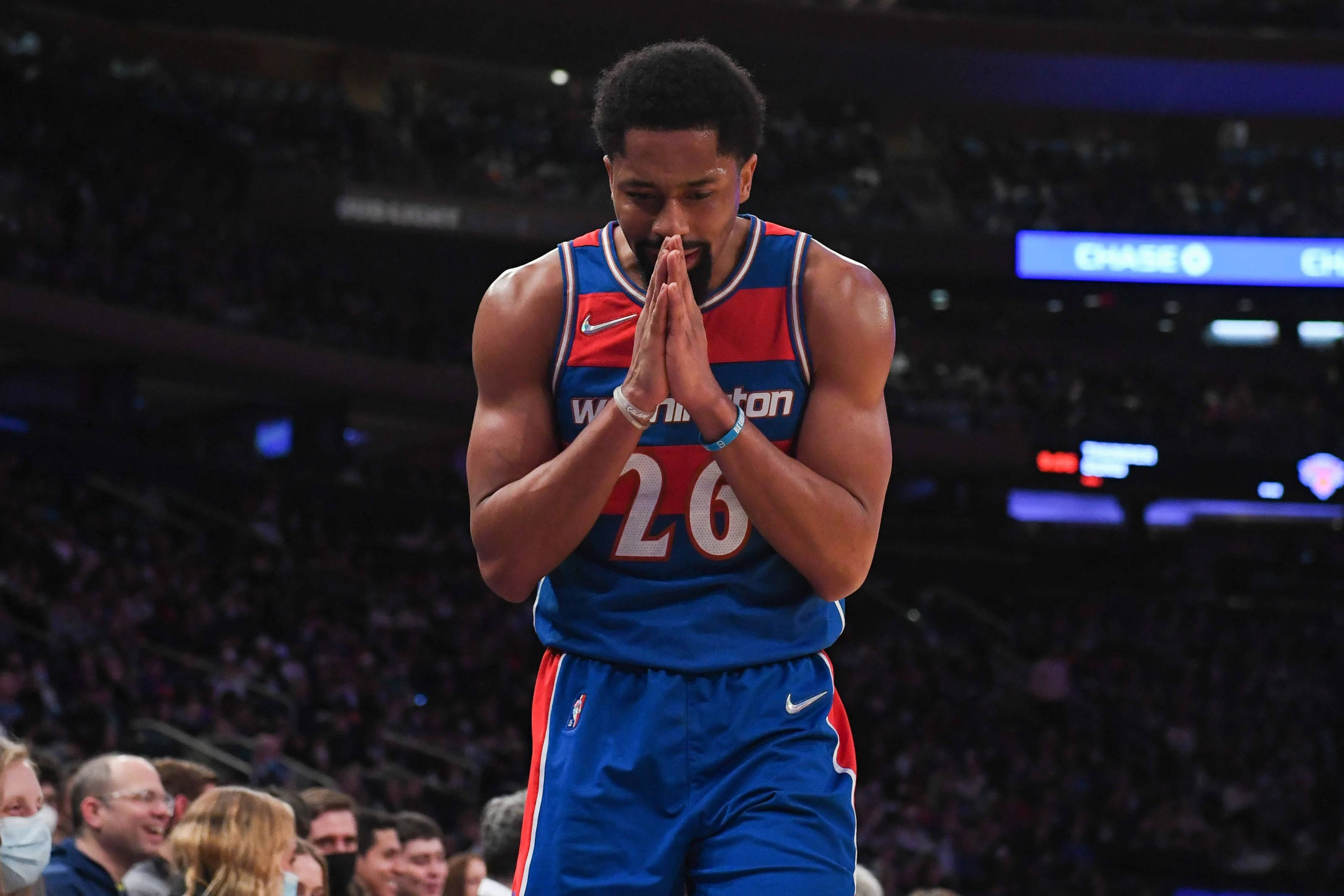 spencer dinwiddie 桌布 壁紙 — 一名身穿藍紅相間華盛頓球衣的籃球運動員在燈光明亮的球場上雙手合十祈禱。