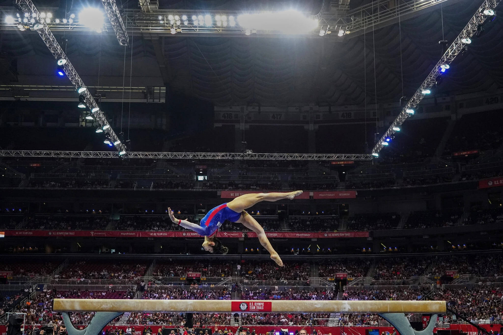 Olympics 桌布 壁紙 — 一名身穿藍紅緊身衣的體操運動員在明亮的場館燈光下，於平衡木上完美翻騰。