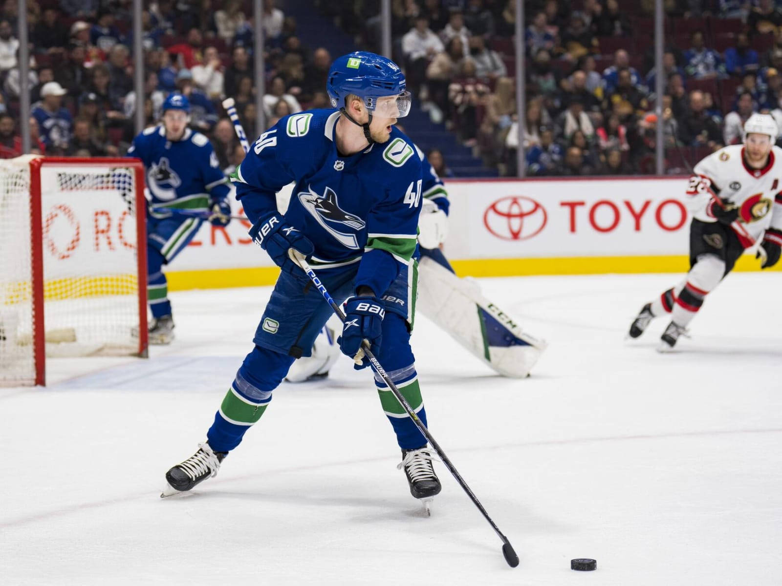 hockey 桌布 壁紙 — 一名身穿藍綠色球衣的冰球運動員在明亮的場館燈光下，於激烈的比賽中帶著冰球滑行。