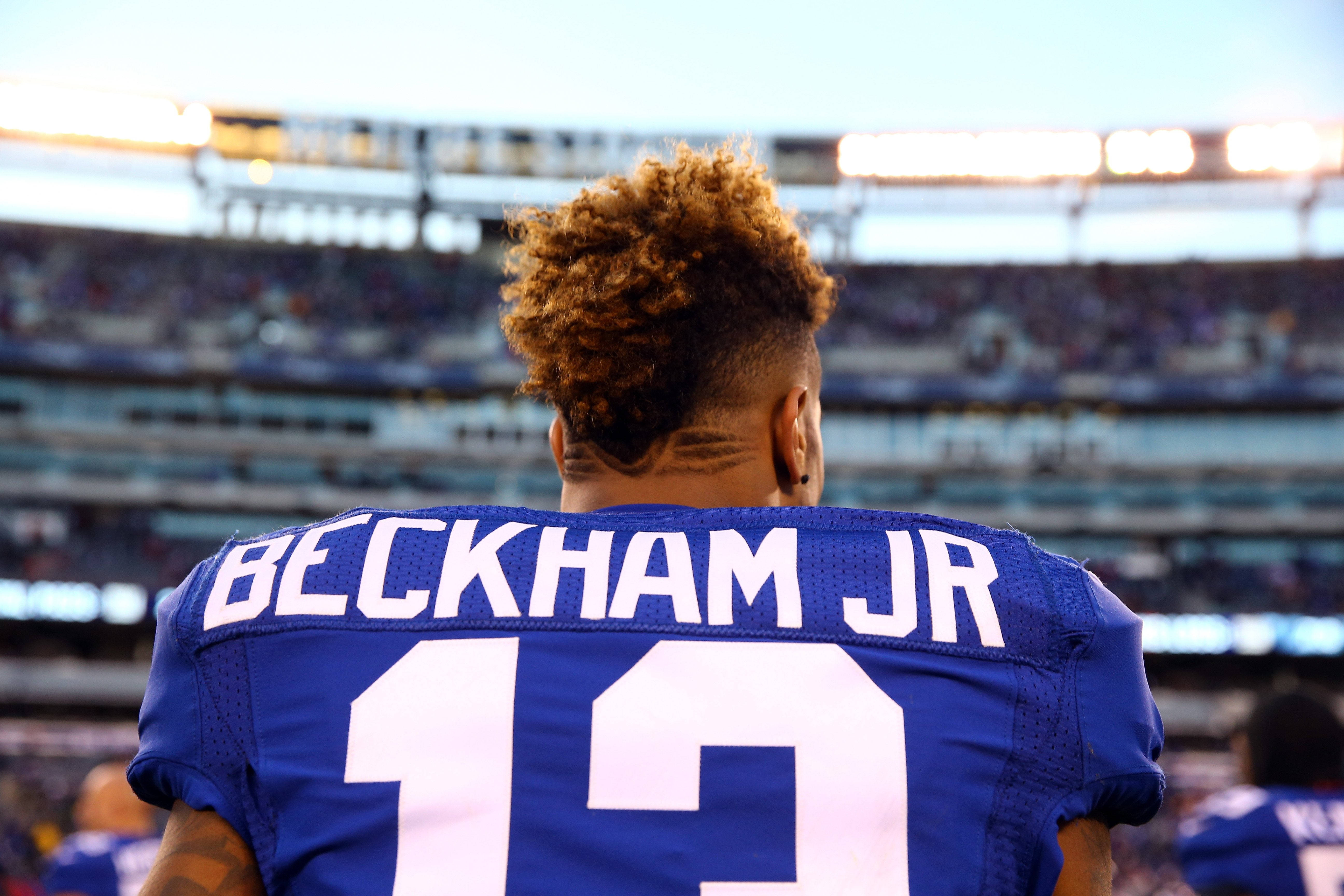 New 桌布 壁紙 — 一名身穿藍色 Beckham Jr 13 球衣的美式足球員背對鏡頭站在夕陽下的球場。