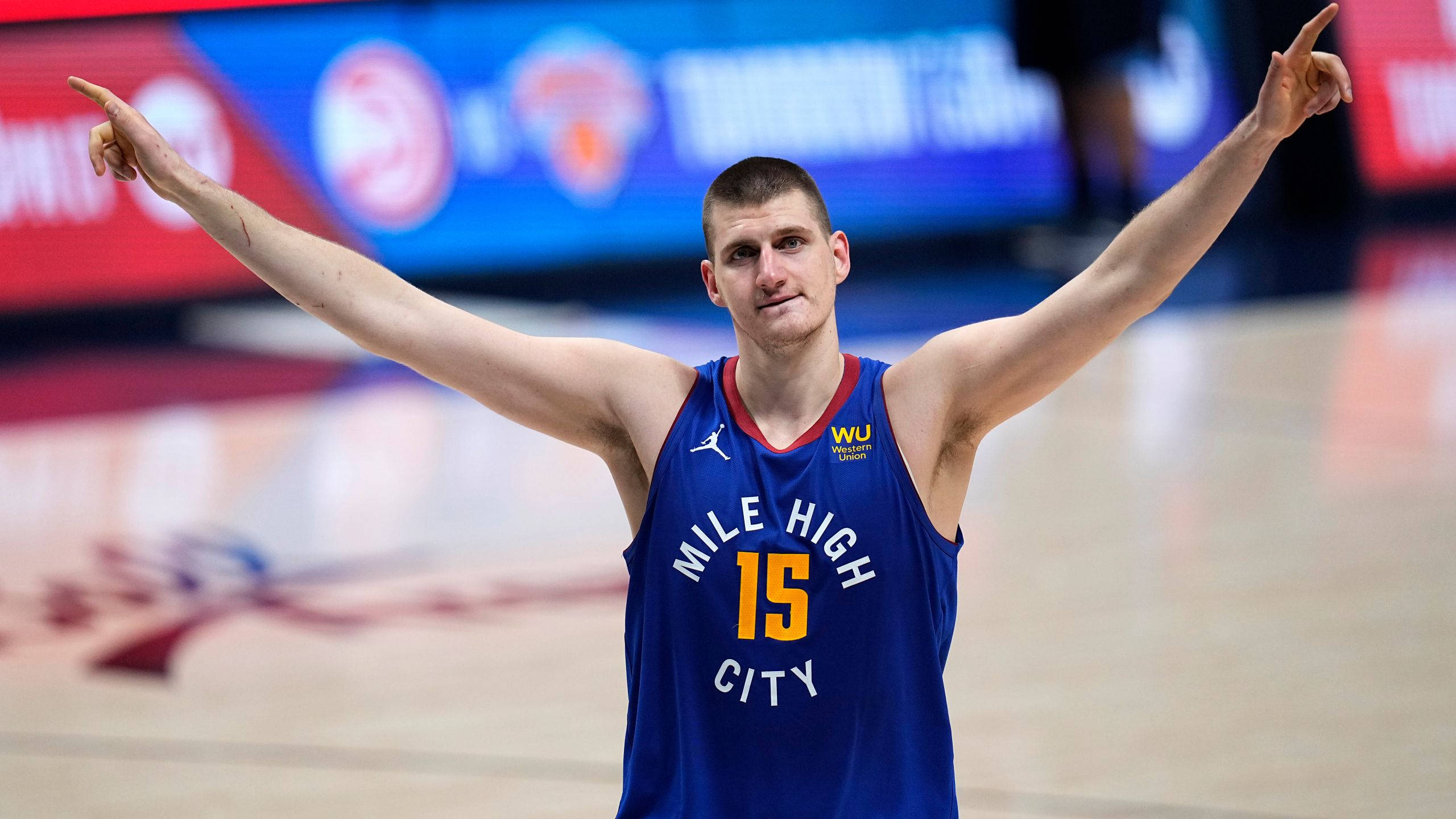 Jokic 桌布 壁紙 — 一名身穿藍色「Mile High City」球衣的籃球運動員在拋光球場上張開雙臂慶祝。