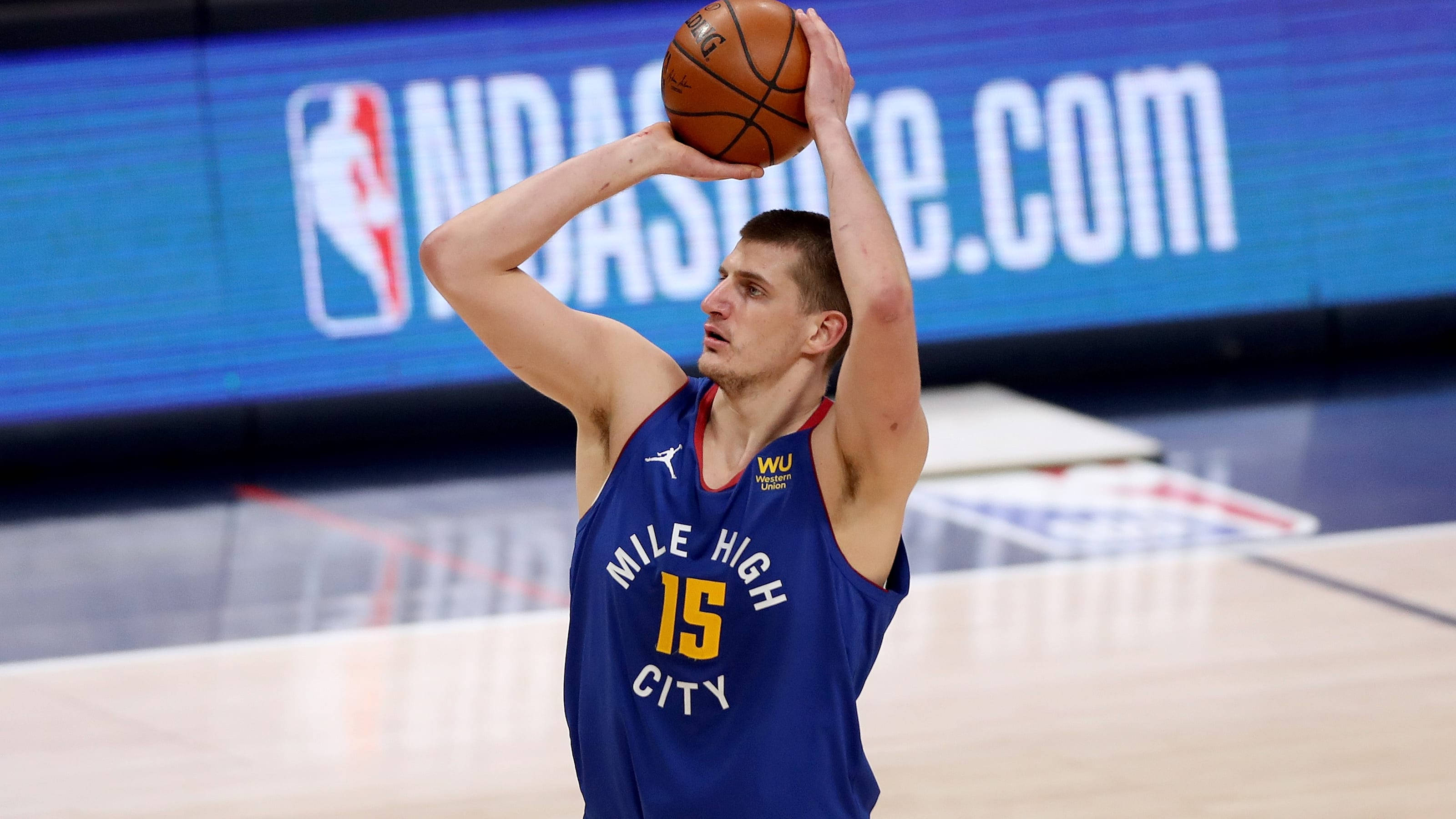 Jokic 桌布 壁紙 — 一名身穿藍色「Mile High City」球衣的籃球運動員在球場上準備投籃，身後有電子計分板。