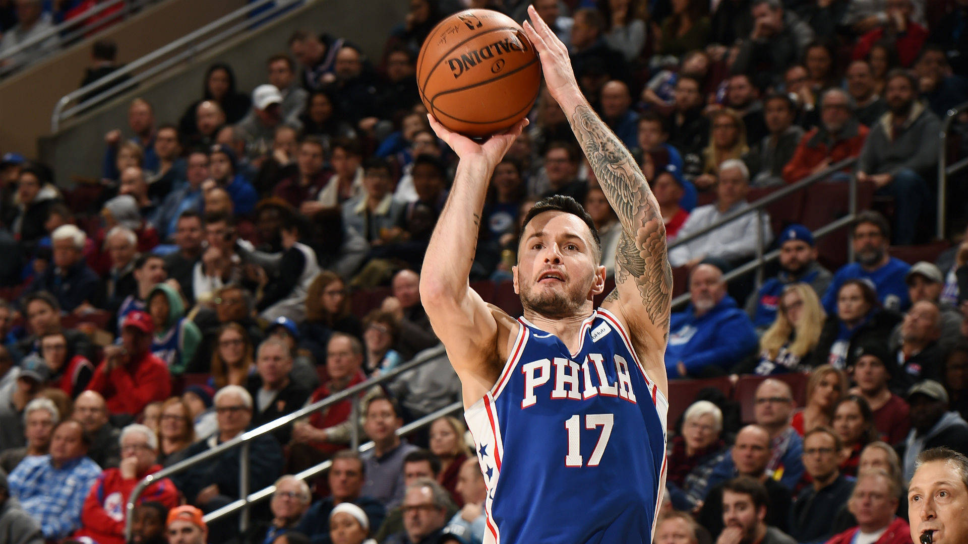 Jj Redick 桌布 壁紙 — 一名身穿藍色 'PHILA' 球衣的籃球運動員，手臂上有可見的刺青，在擠滿觀眾的場館中投籃。