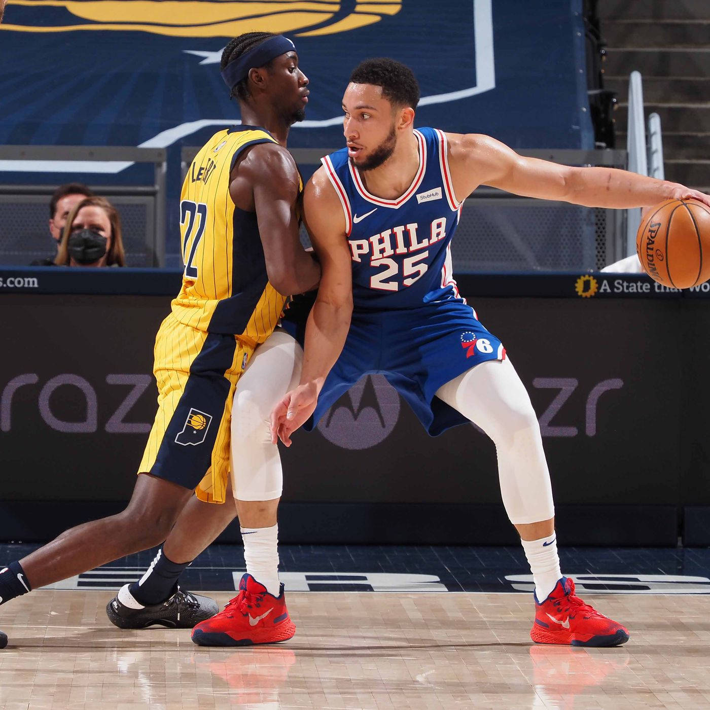 caris levert 桌布 壁紙 — 一名身穿藍色 'PHILA' 球衣的籃球運動員在激烈的比賽中運球，同時被一名身穿黃色條紋球衣的對手緊密防守。
