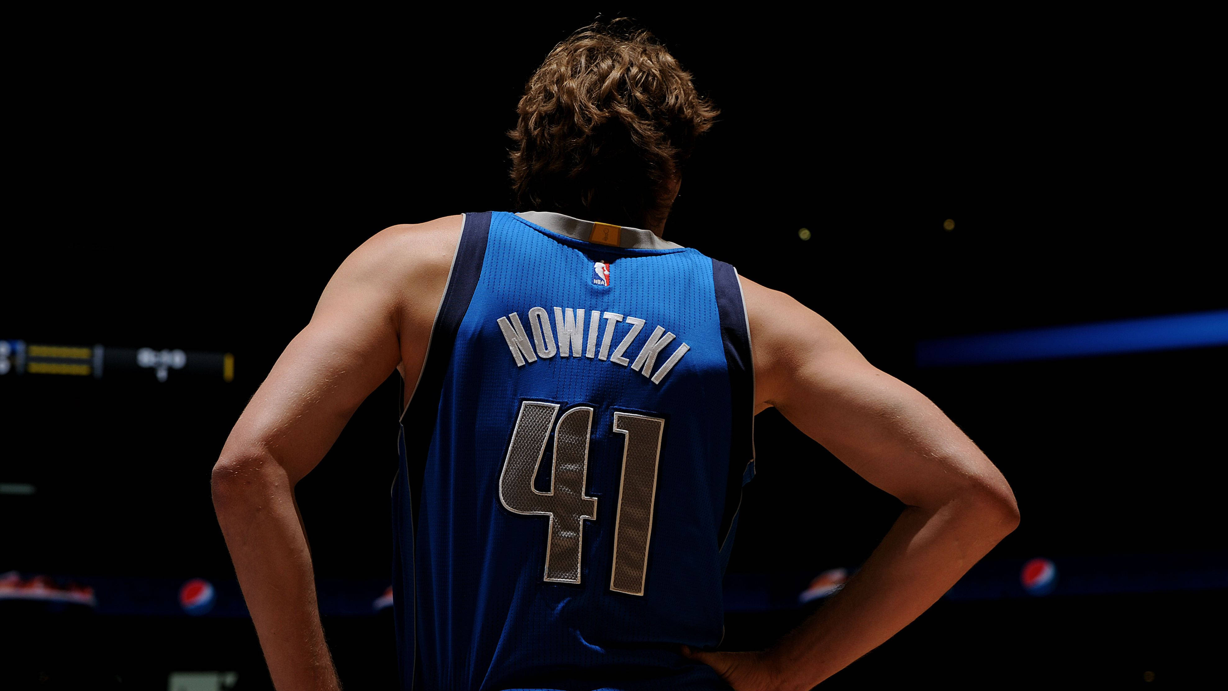 Dirk Nowitzki 桌布 壁紙 — 一名身穿藍色Nowitzki 41球衣的籃球運動員在場館燈光下雙手叉腰背對鏡頭站立。