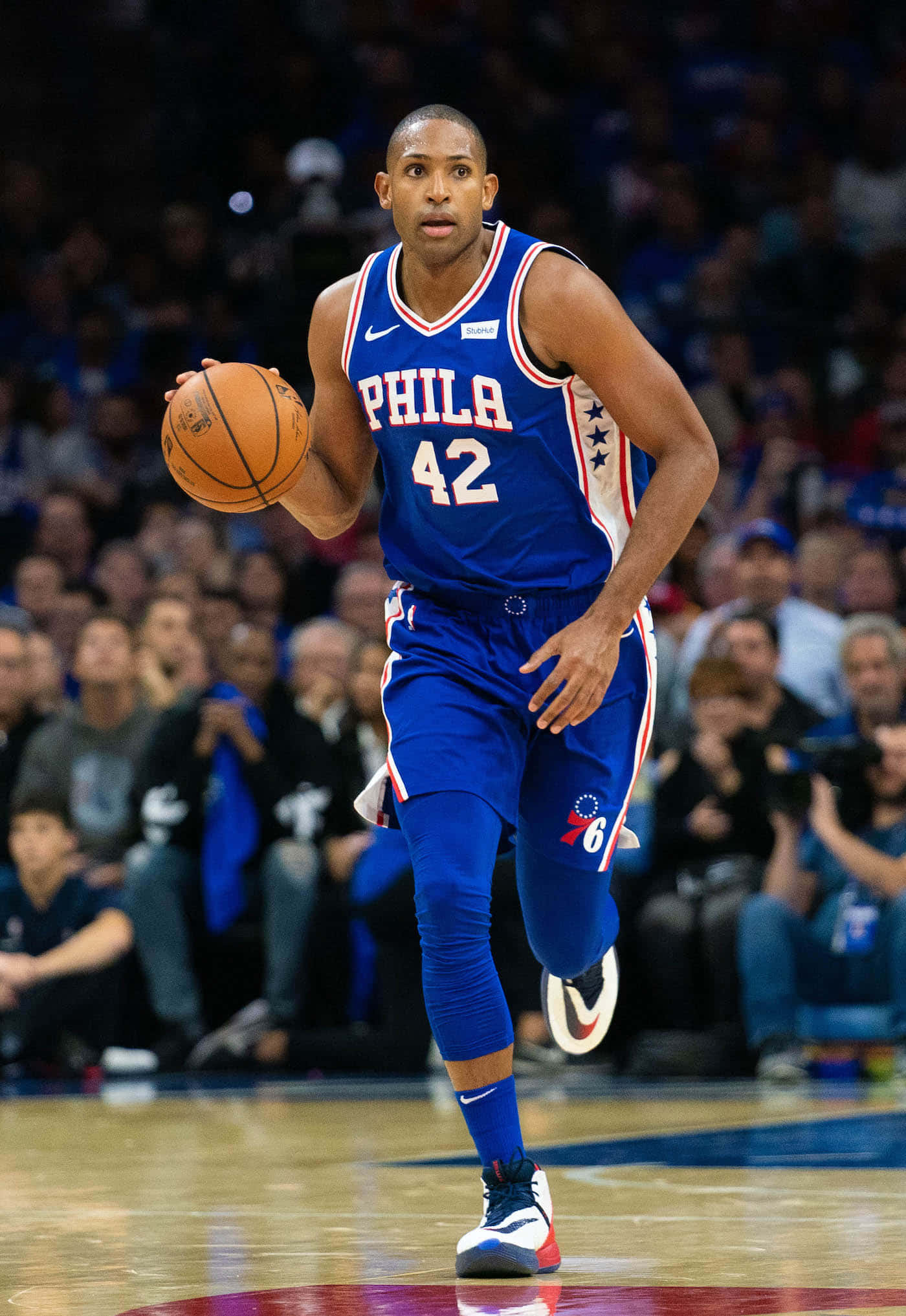 Al Horford 桌布 壁紙 — 一名身穿藍色Phila 42球衣的籃球運動員在明亮的場館燈光下，於激烈的比賽中運球。
