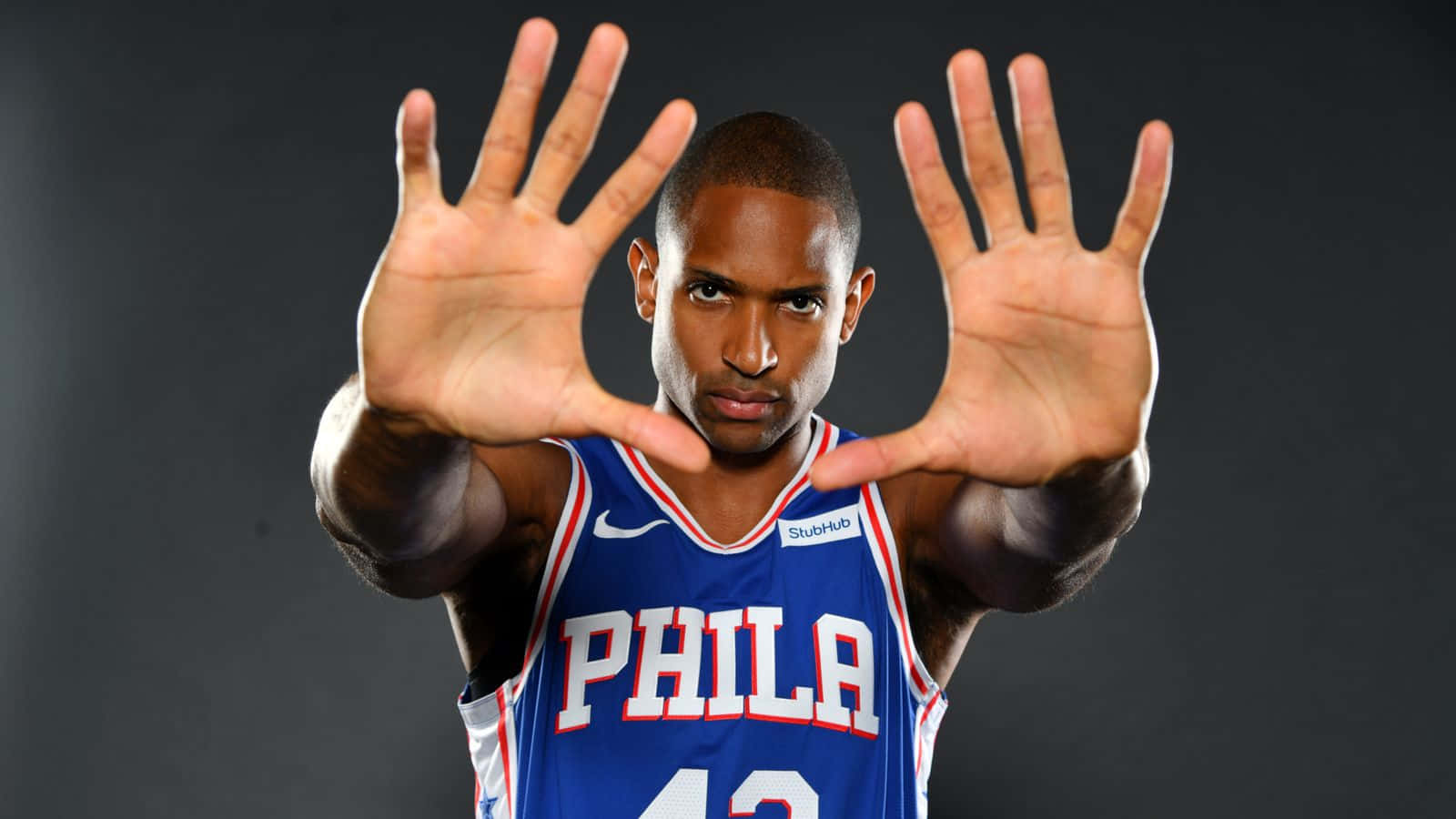 Al Horford 桌布 壁紙 — 一名身穿藍色Phila球衣的籃球運動員在深色攝影棚背景下雙手向前伸出。