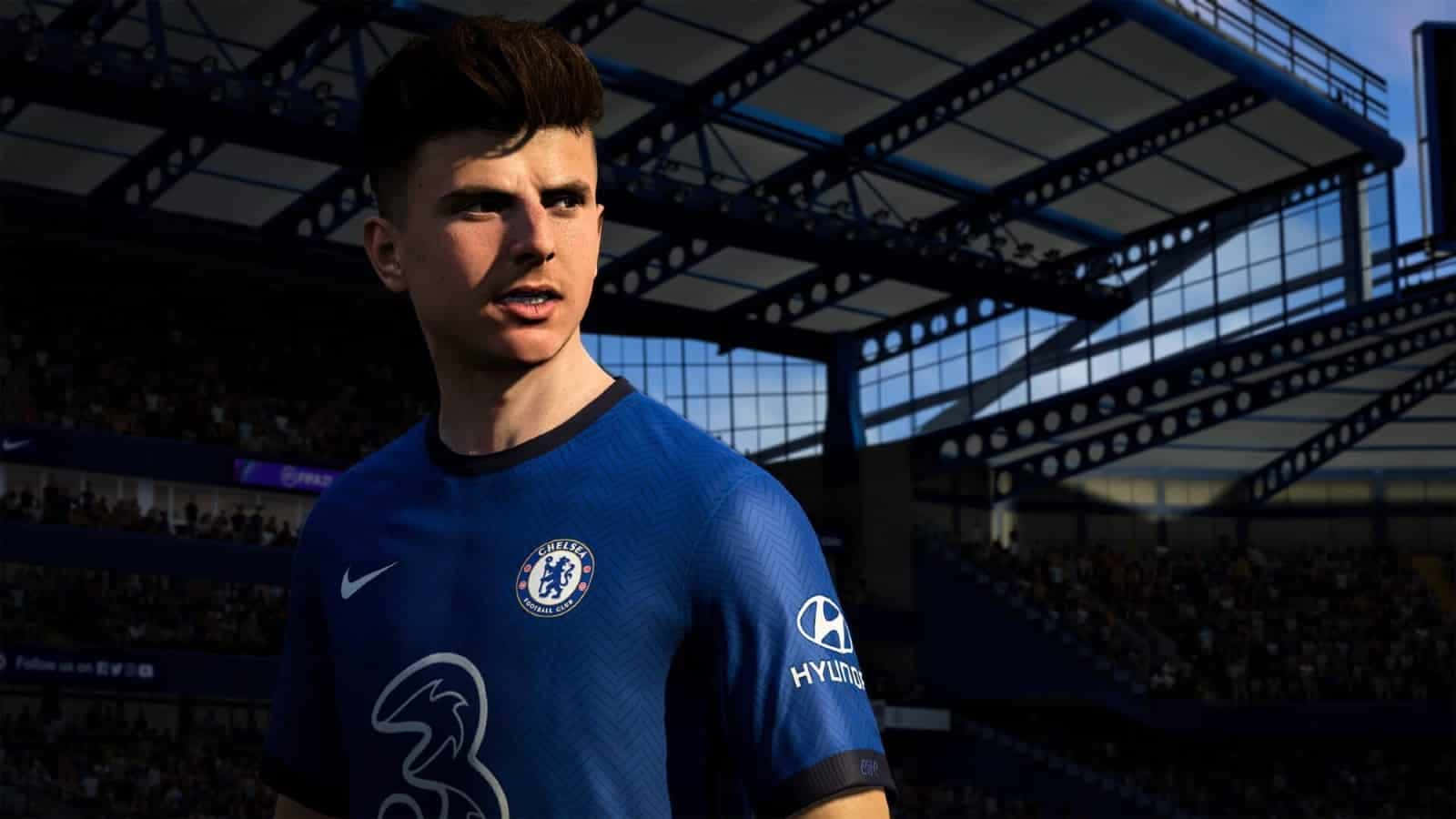 Fifa 22 桌布 壁紙 — 一名身穿藍色切爾西球衣的足球員站在球場上，球迷和明亮的陽光在看台上投下陰影。