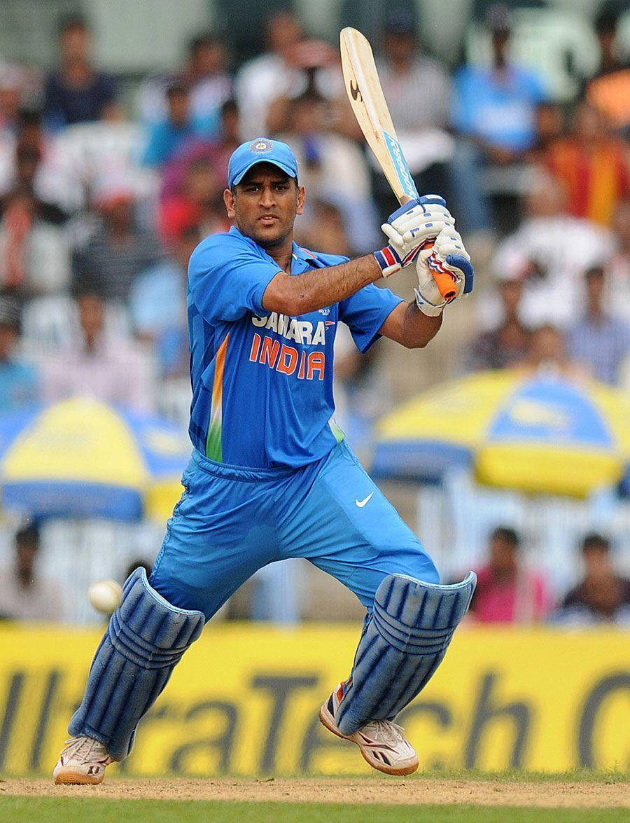 Ms Dhoni 桌布 壁紙 — 一名身穿藍色印度隊服的板球運動員在日間比賽中專注地揮動球棒。