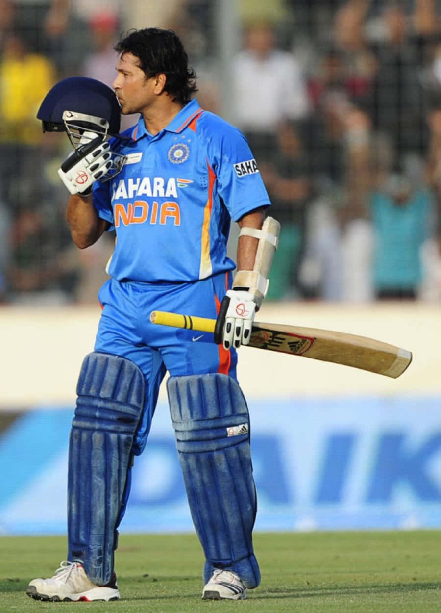 Sachin Tendulkar 桌布 壁紙 — 一名身穿藍色印度隊服的板球運動員在球場燈光下的綠色場地上手持頭盔和球棒。