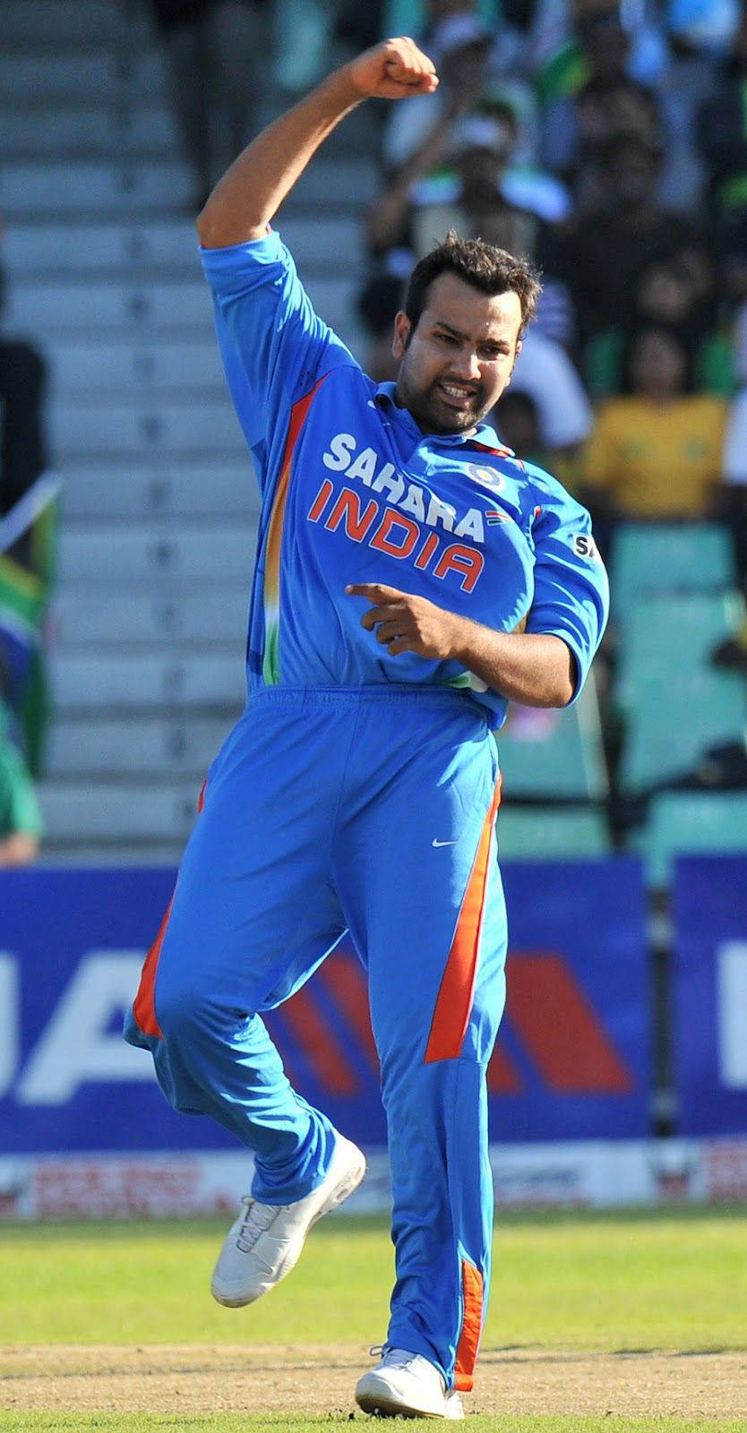 Rohit Sharma 桌布 壁紙 — 一名身穿藍色印度隊服的板球運動員在陽光明媚的綠色球場上舉起拳頭慶祝。