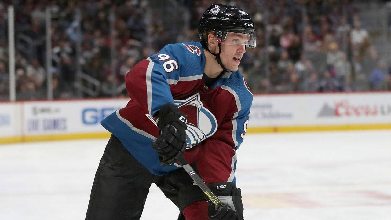 hockey 桌布 壁紙 — 一名身穿藍色和栗色球衣的冰球運動員在比賽中，在人群背景下，在冰上激烈地向前傾身。