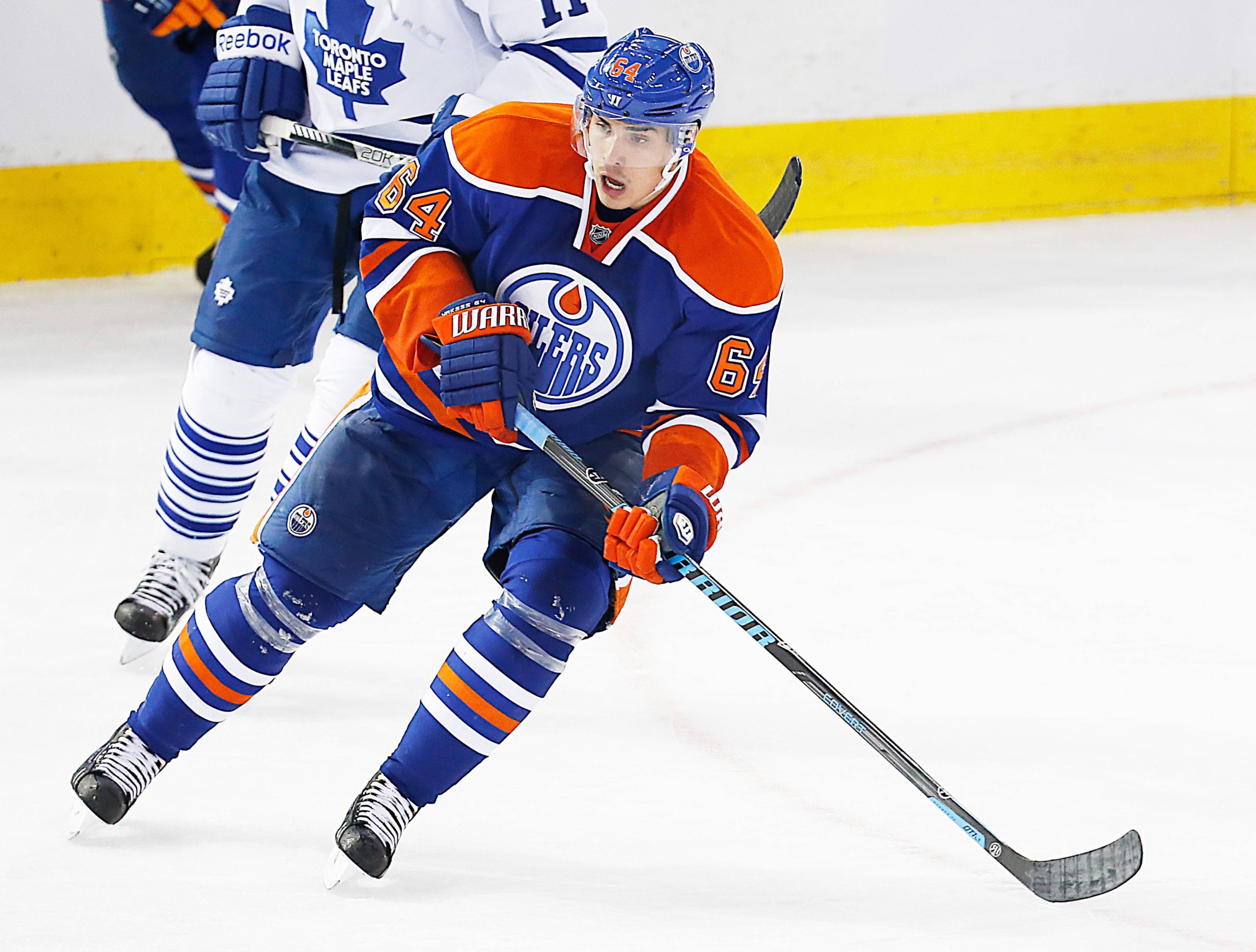 Oilers 桌布 壁紙 — 一名身穿藍色和橙色愛德蒙頓油人隊裝備的冰球運動員在比賽中於冰上激烈滑行，多倫多楓葉隊球員在後追趕。