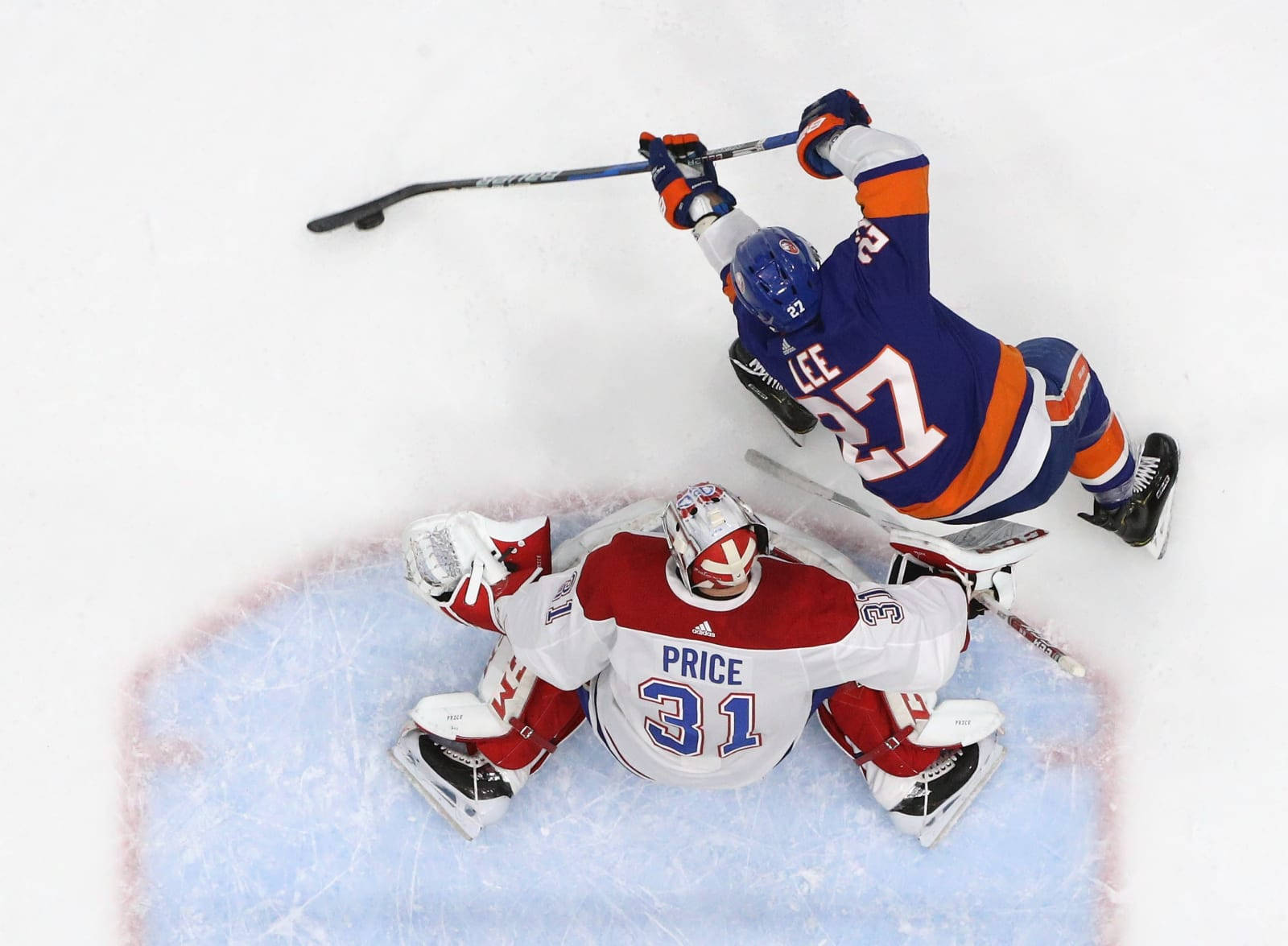 New York Islanders 桌布 壁紙 — 一名身穿藍色和橙色球衣的冰球運動員向球門飛撲，而身穿紅色和白色球衣的守門員在冰上伸展身體試圖擋住射門。