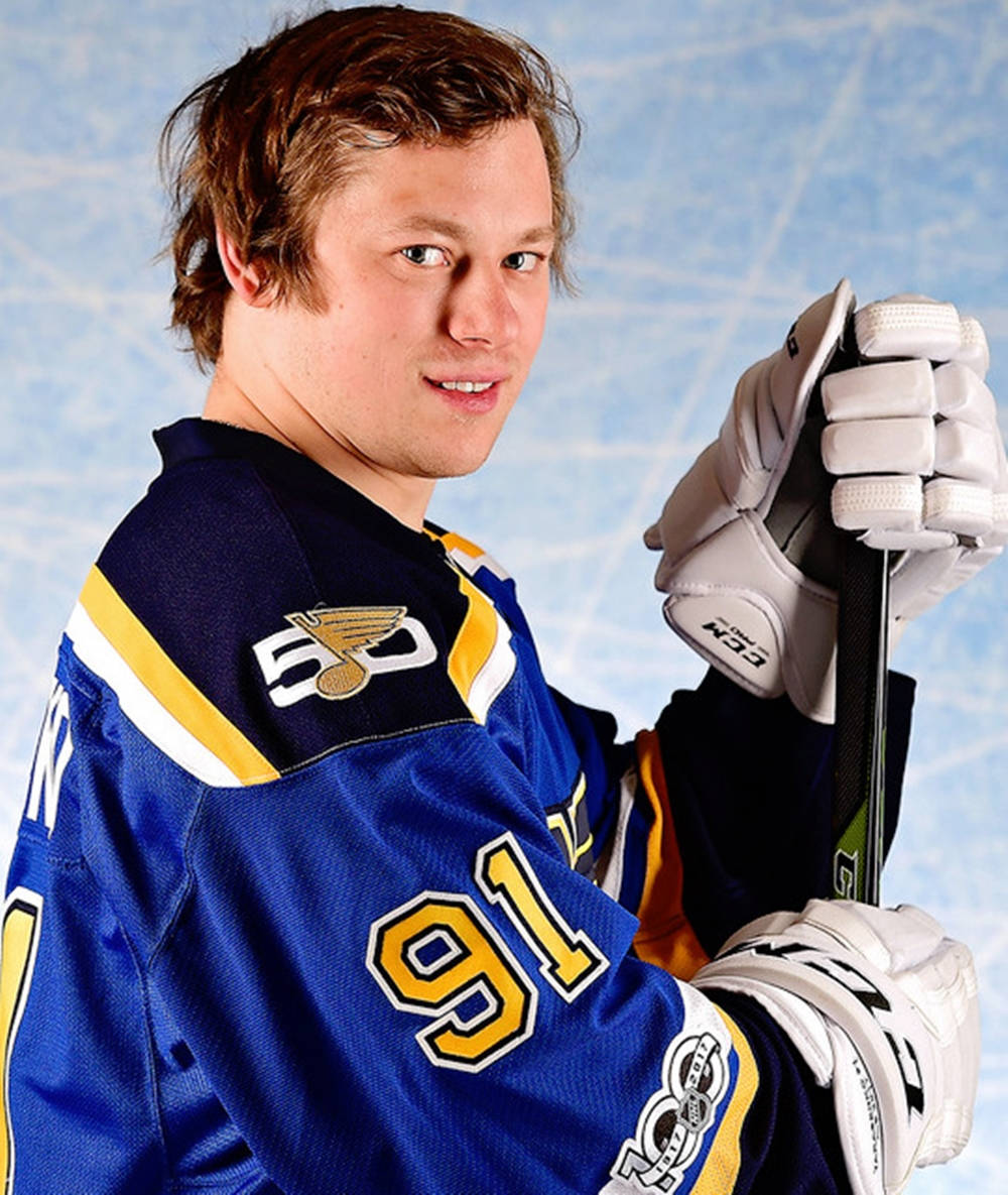 St Louis Blues 桌布 壁紙 — 一名身穿藍色和金色球衣、號碼91的冰球運動員，在模糊的冰場背景下拿著球桿。