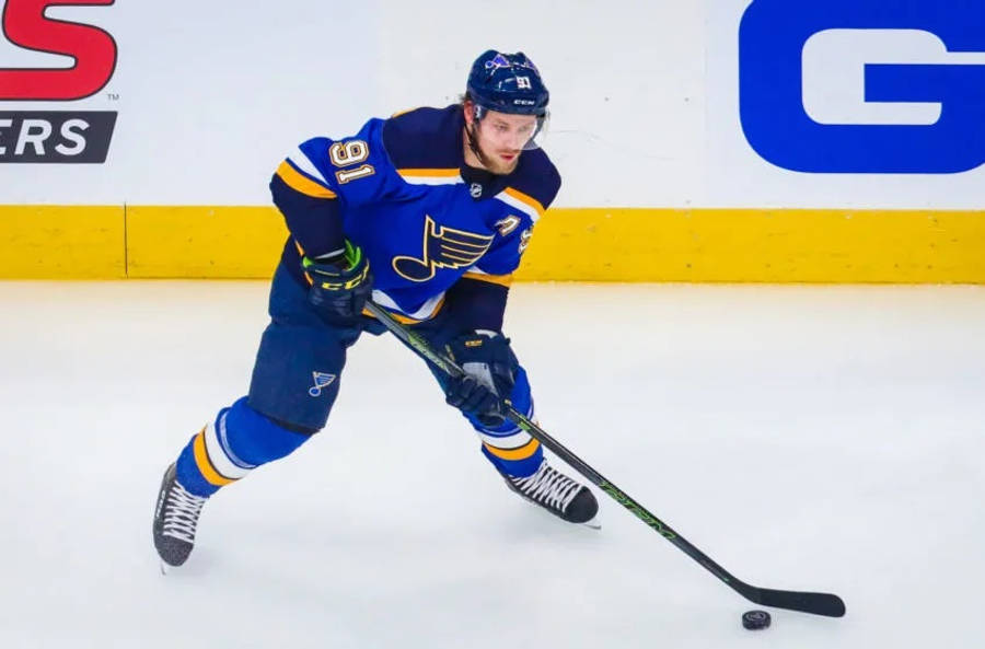 St Louis Blues 桌布 壁紙 — 一名身穿藍色和金色球衣的冰球運動員在比賽中帶著球桿和冰球在冰上激烈滑行。
