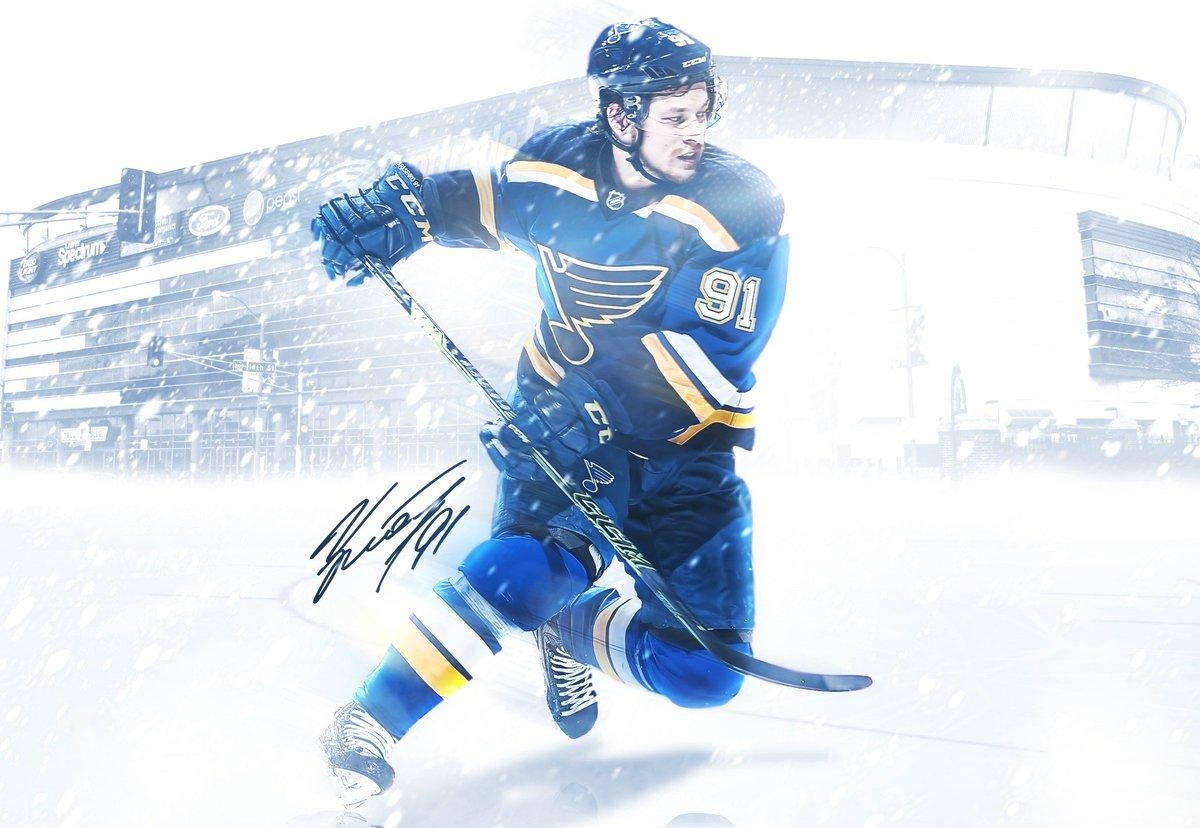 St Louis Blues 桌布 壁紙 — 一名身穿藍色和金色球衣的冰球運動員在冰場上，背景是體育館，動態地滑過飄落的雪花。