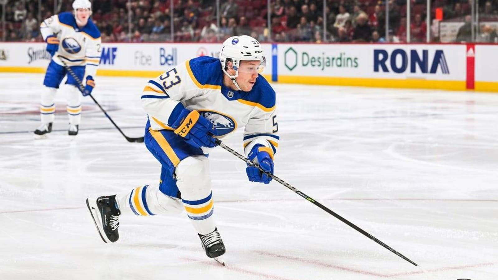 hockey 桌布 壁紙 — 一名身穿藍色和金色球衣的冰球運動員在明亮的場館燈光下，在比賽中帶著冰球在冰上激烈滑行。