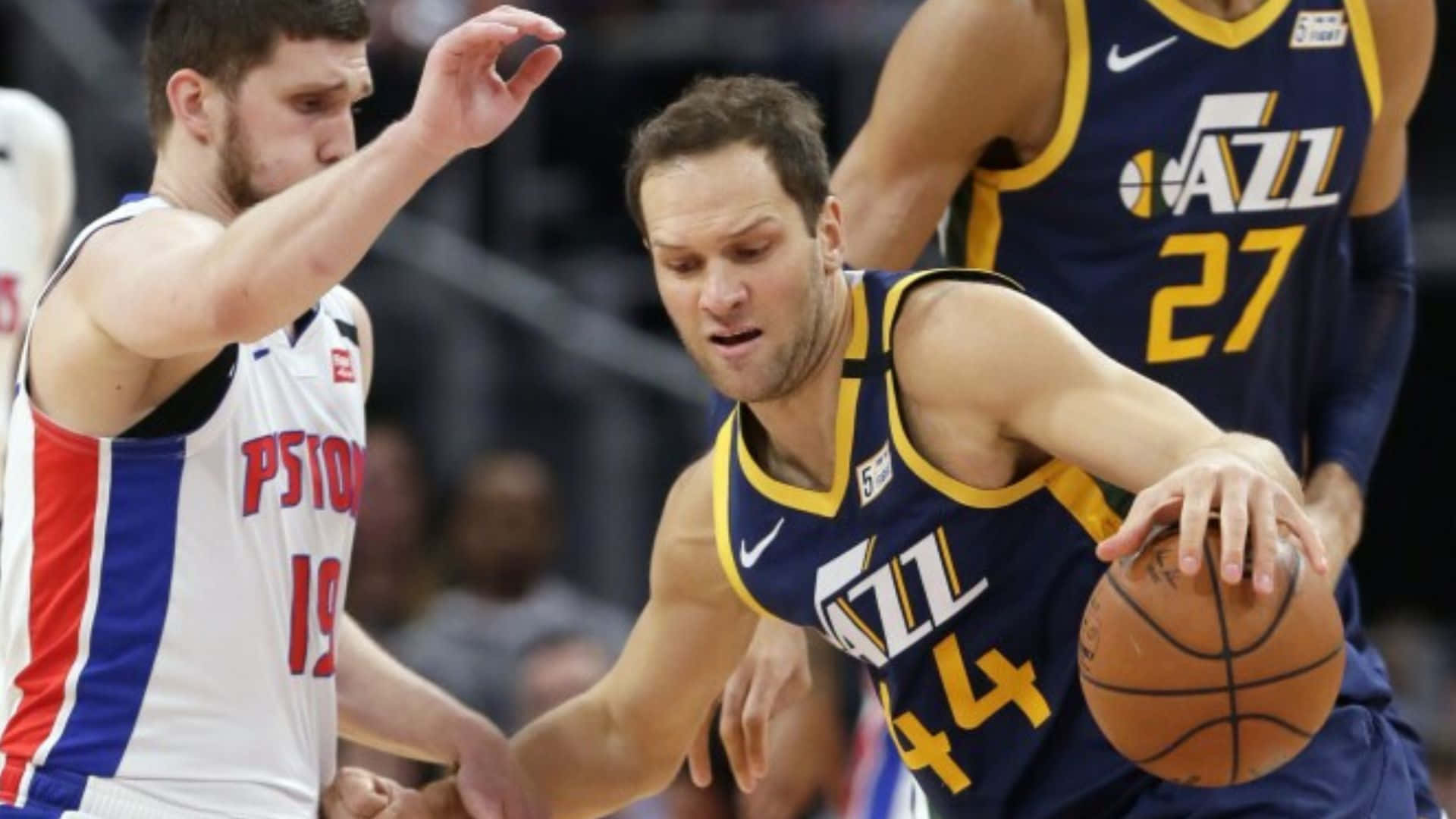 NBA 桌布 壁紙 — 一名身穿藍色和金色球衣的猶他爵士隊球員運球，同時被一名身穿白、紅、藍色的底特律活塞隊球員緊密防守。