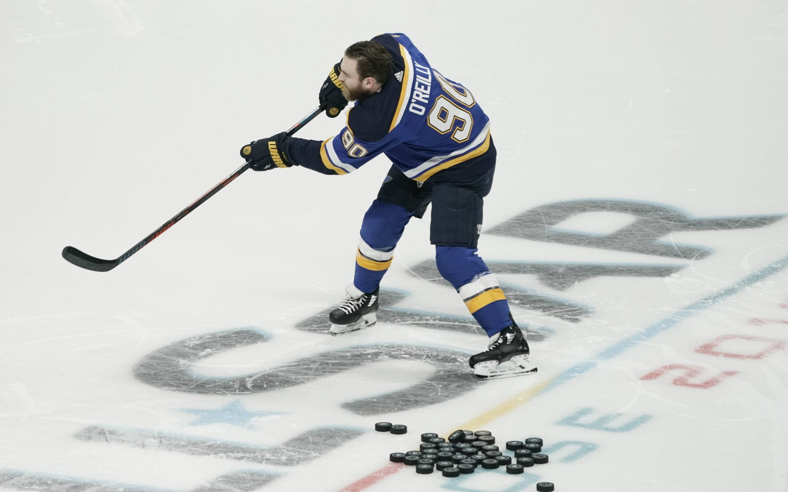 hockey 桌布 壁紙 — 一名身穿藍色和金色裝備的冰球運動員在冰上向前傾，在散落的冰球附近拿著球桿。