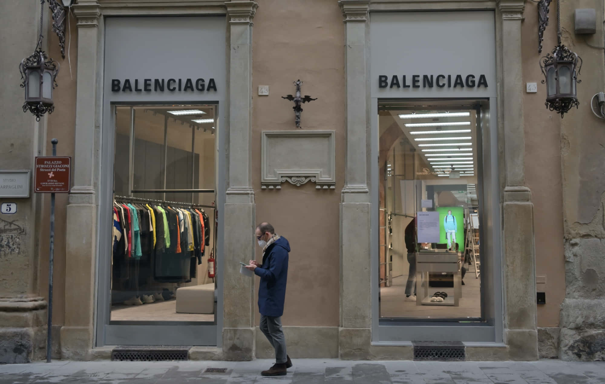 巴黎世家 桌布 壁紙 — 一名身穿藍色外套和口罩的男子走過 Balenciaga 商店，櫥窗內展示著色彩繽紛的服裝。