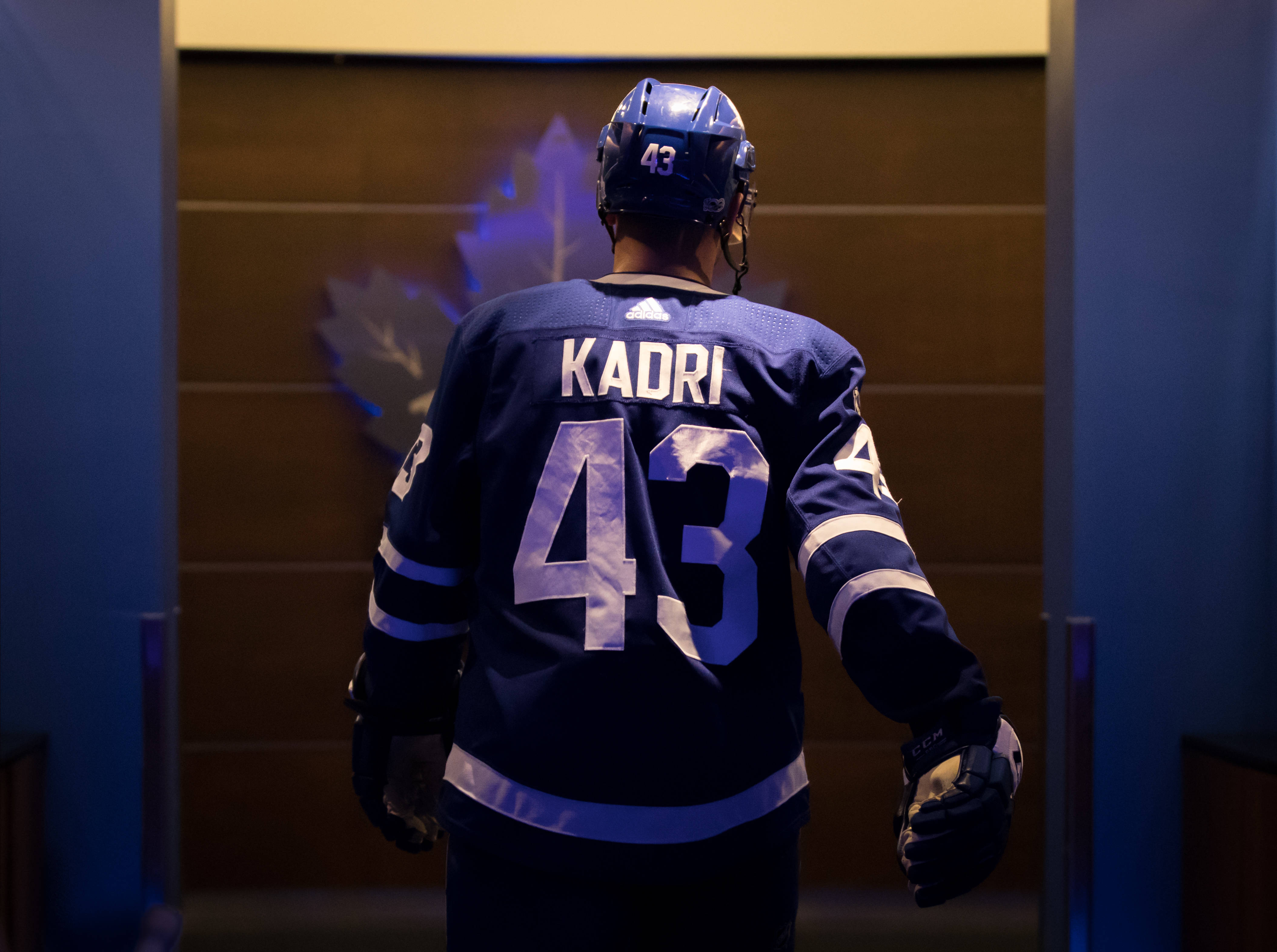 hockey 桌布 壁紙 — 一名身穿藍色多倫多楓葉隊球衣的冰球運動員，沿著燈光昏暗的走廊走向牆上發光的楓葉標誌。