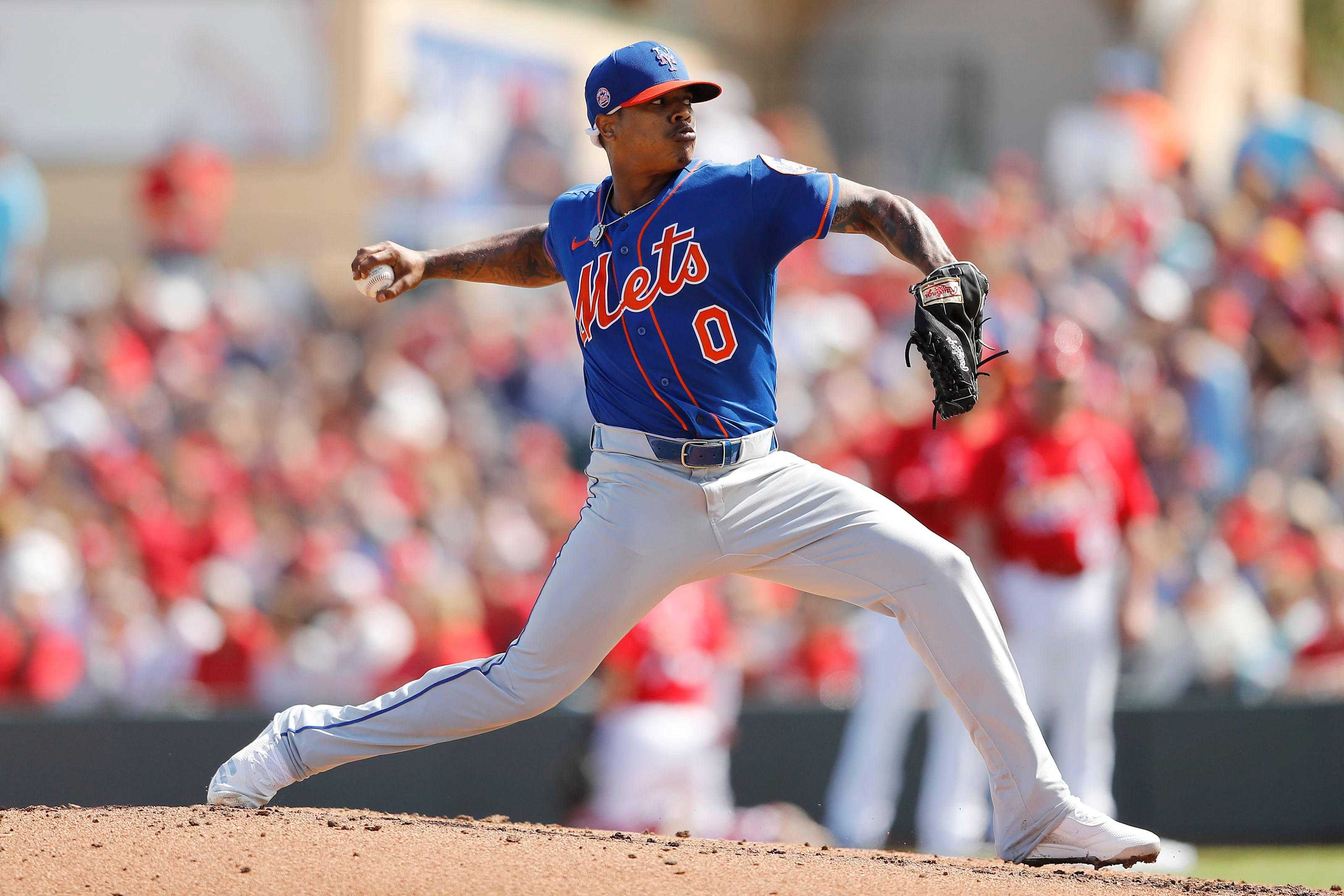 Marcus Stroman 桌布 壁紙 — 一名身穿藍色大都會隊球衣的棒球投手在陽光照耀的投手丘上投球，背景是模糊的人群。