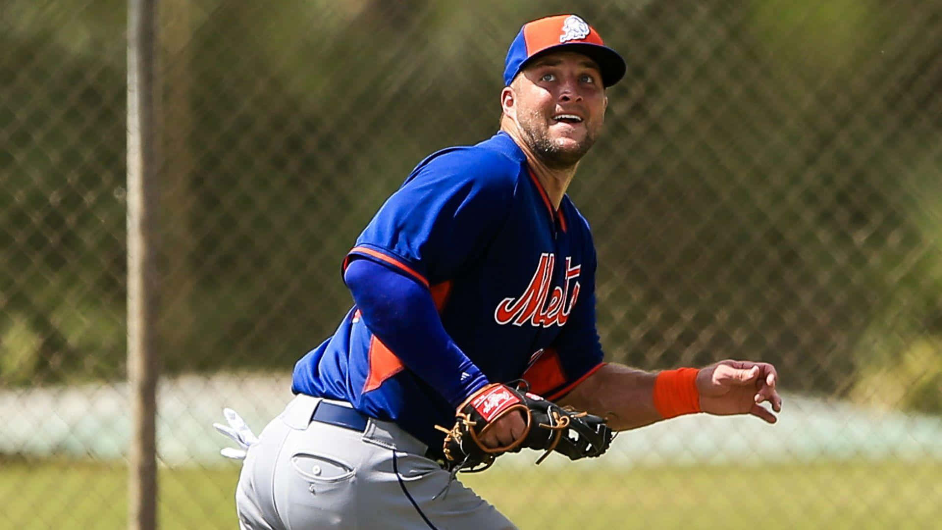 Tim Tebow 桌布 壁紙 — 一名身穿藍色大都會隊球衣的棒球運動員在陽光明媚的戶外練習中，戴著手套向前猛撲。