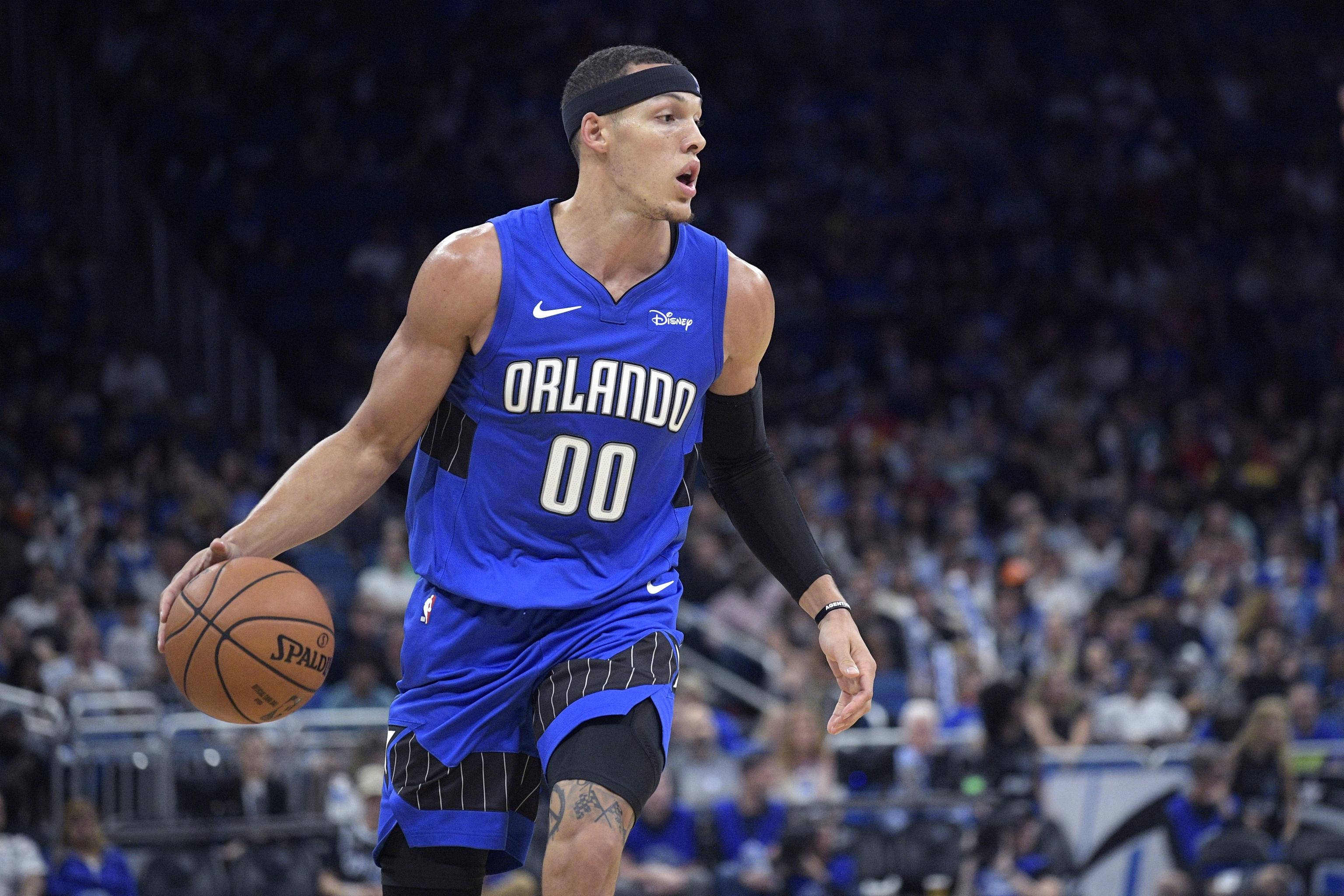 aaron gordon 桌布 壁紙 — 一名身穿藍色奧蘭多球衣的籃球運動員在比賽中運球，背景是模糊的人群。