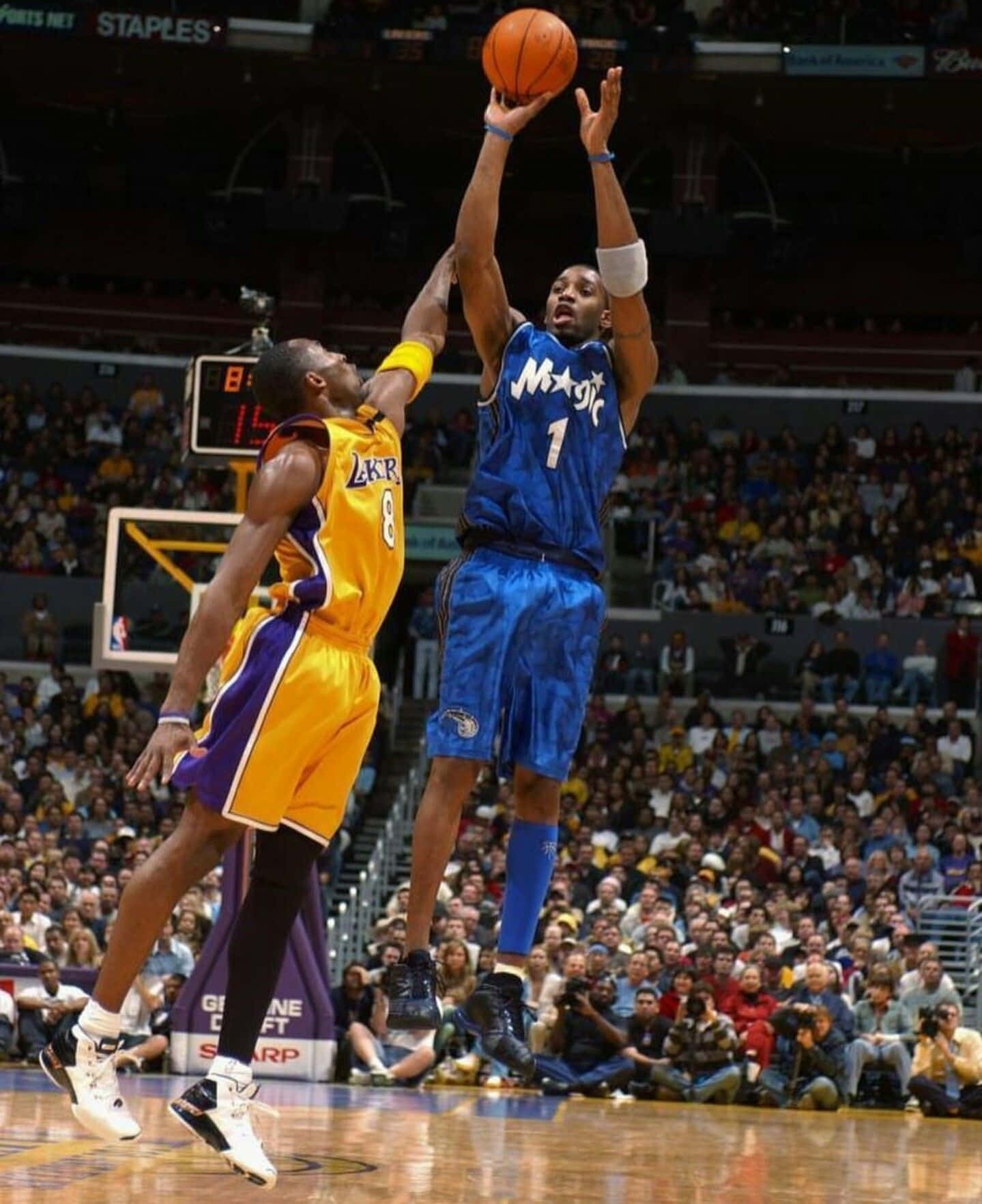 Tracy Mcgrady 桌布 壁紙 — 一名身穿藍色奧蘭多魔術隊球衣的籃球運動員跳起投籃，而一名身穿黃色的湖人隊防守球員試圖封阻。