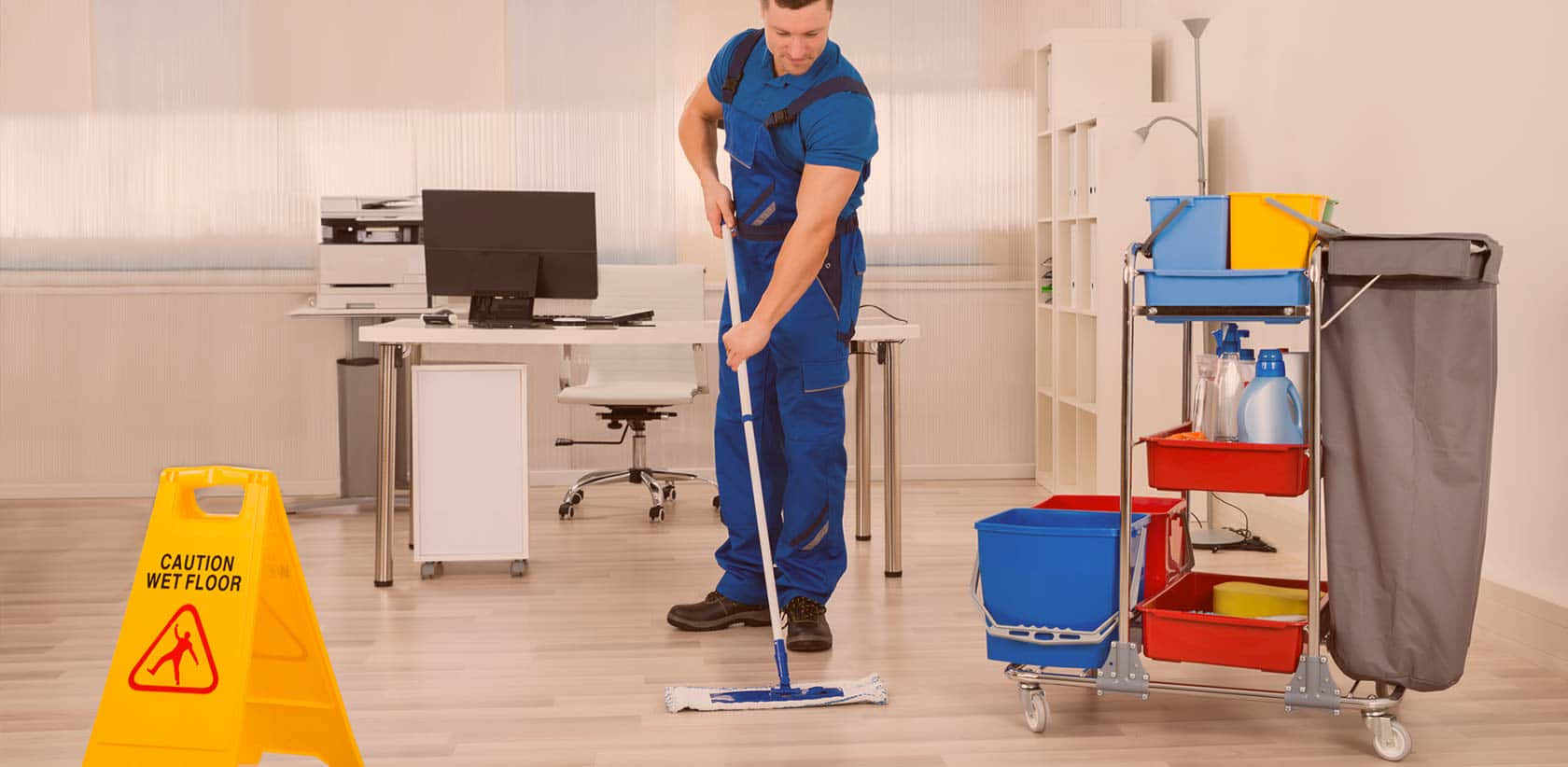 Cleaning 桌布 壁紙 — 一名身穿藍色工作服的清潔工正在清潔的辦公室地板上拖地，旁邊有一個黃色濕滑地板標誌和清潔手推車。