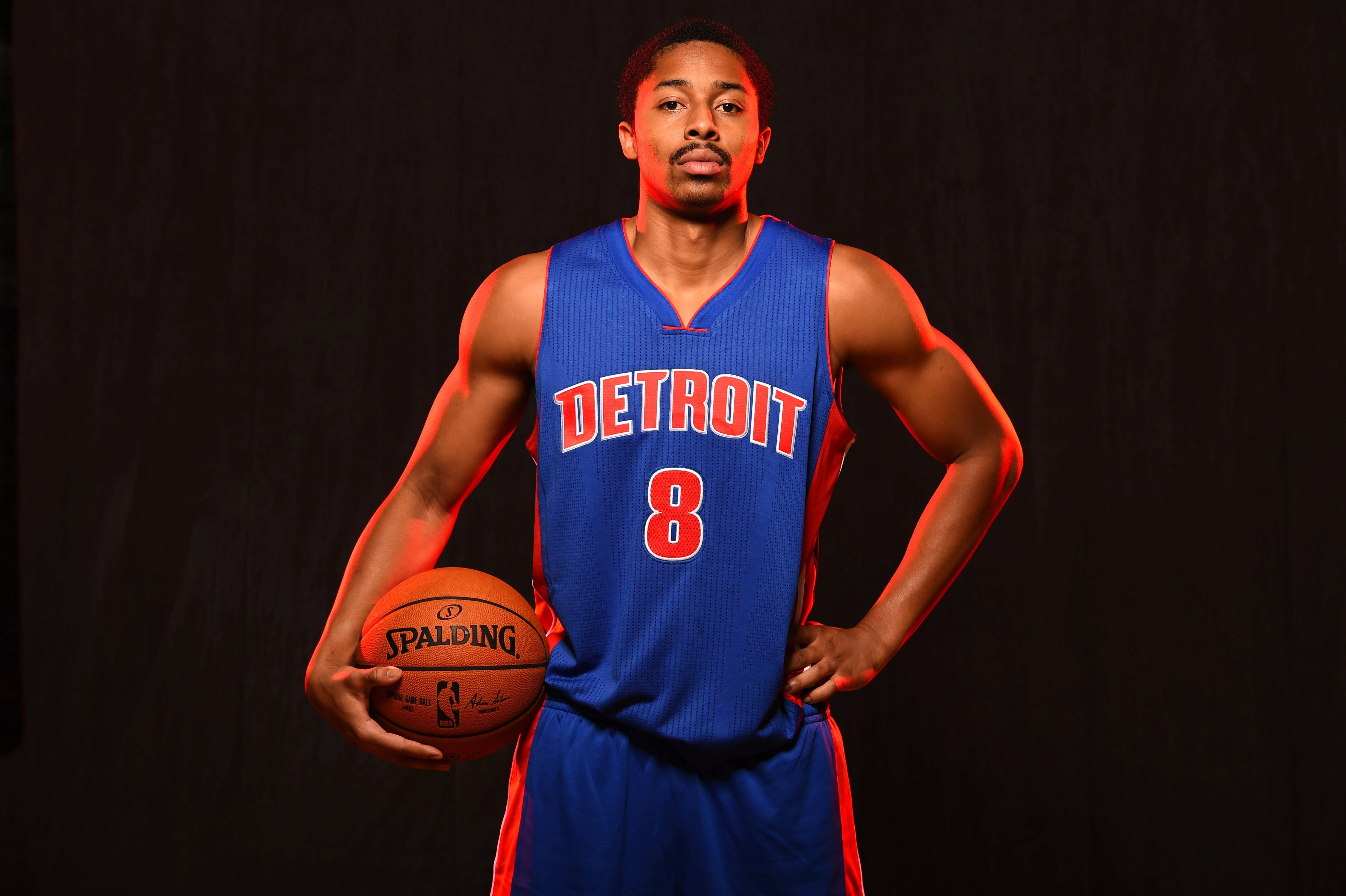 spencer dinwiddie 桌布 壁紙 — 一名身穿藍色底特律球衣、背號8的籃球運動員自信地站立，手持Spalding籃球，背景為深色並帶有紅色燈光點綴。
