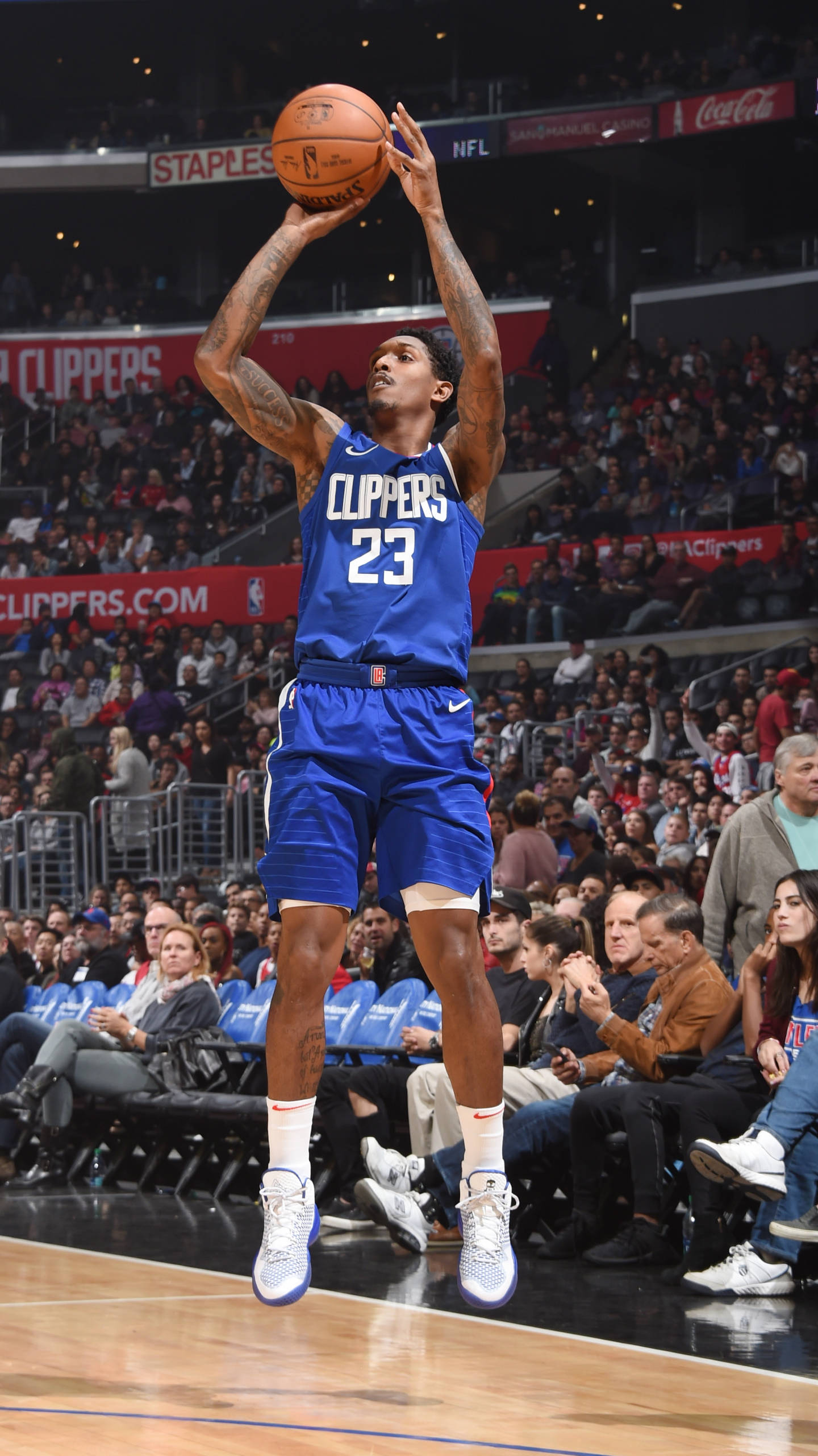 Lou Williams 桌布 壁紙 — 一名身穿藍色快艇隊球衣的籃球運動員在明亮的燈光下，在擠滿觀眾的場館中跳起投籃。