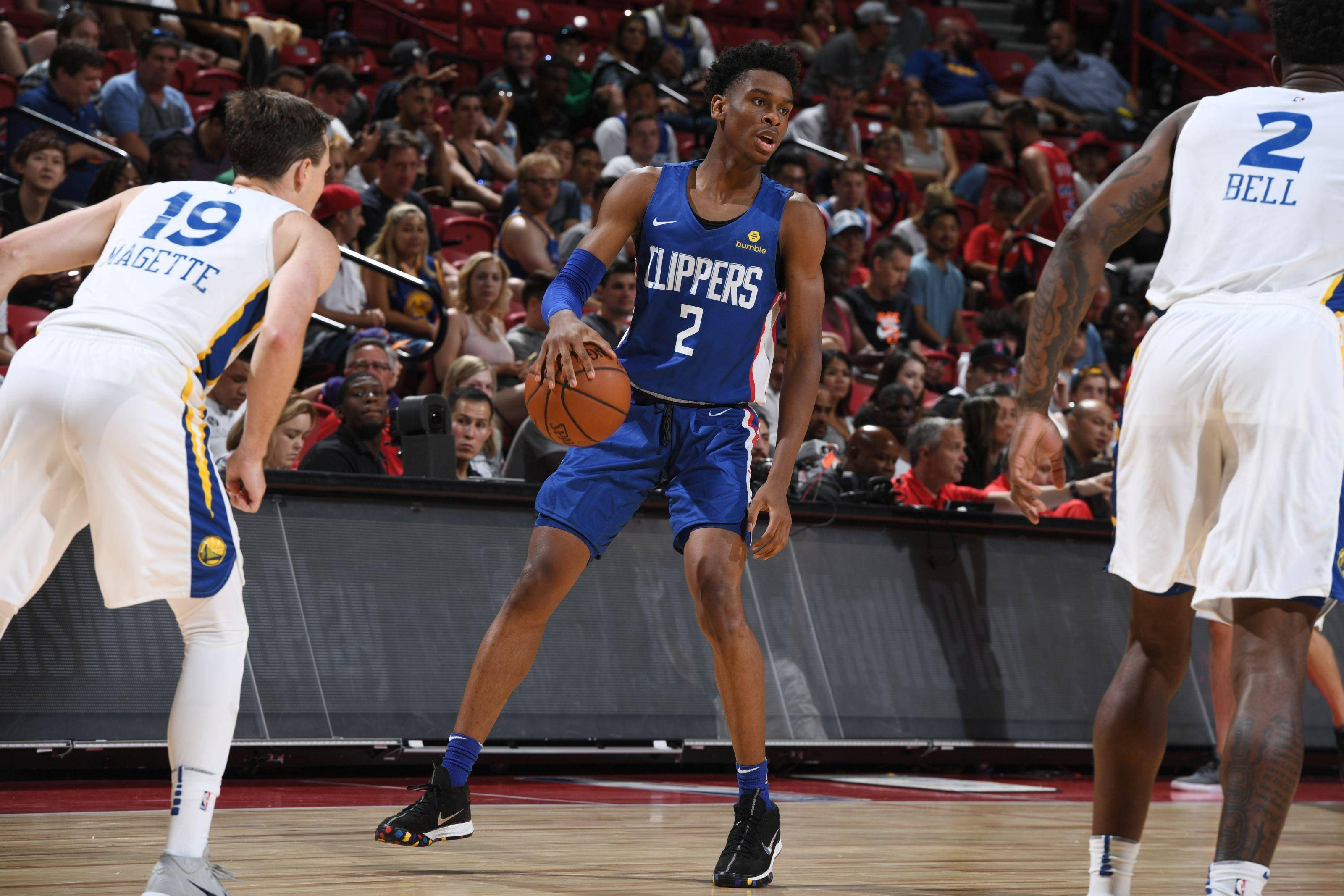 Shai Gilgeous Alexander 桌布 壁紙 — 一名身穿藍色快艇隊球衣的籃球運動員在擠滿觀眾的場館中運球，同時被兩名對手防守。