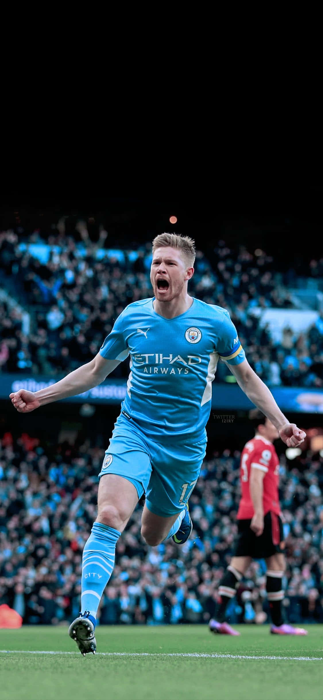Manchester City iPhone 桌布 壁紙 — 一名身穿藍色曼城球衣的足球員在燈光璀璨的球場上張開雙臂慶祝進球。