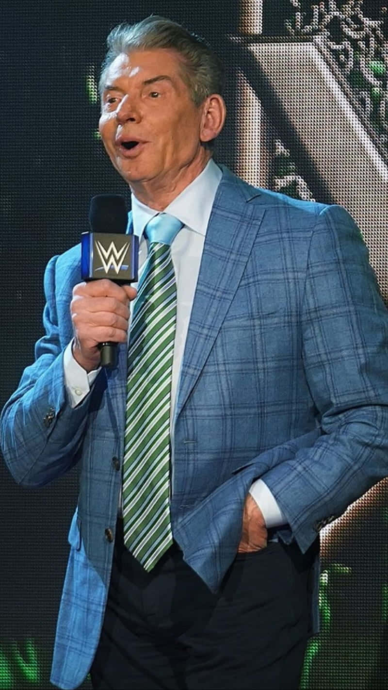 WWE 桌布 壁紙 — 一名身穿藍色格紋西裝和綠色條紋領帶的男子，在明亮的燈光下於舞台上拿著WWE麥克風說話。