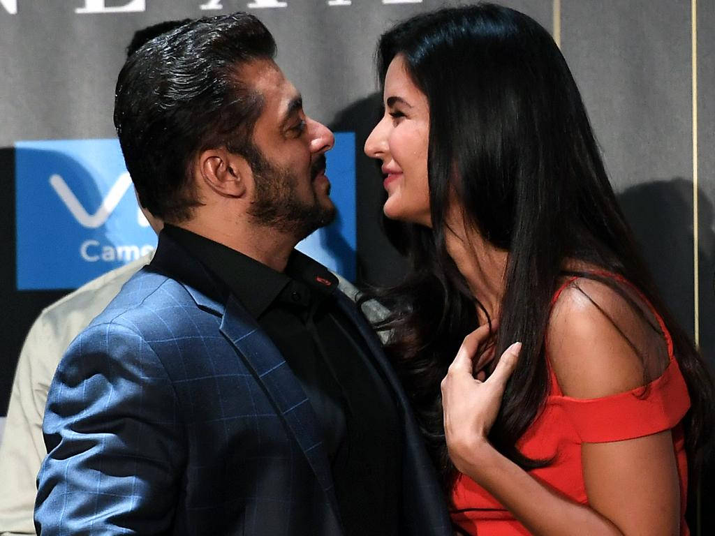 salman khan HD 桌布 壁紙 — 一名身穿藍色格紋西裝的男子和一名身穿紅色連衣裙的女子在帶有品牌背景的新聞發布會上分享親密時刻。