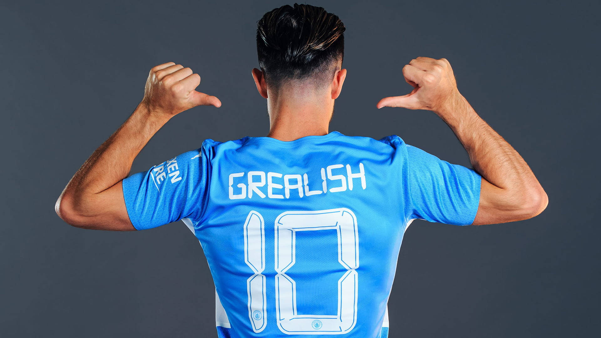 足球 桌布 壁紙 — 一名身穿藍色球衣、背後印有「GREALISH 10」的足球運動員，在深灰色工作室背景下彎曲手臂展示身材。