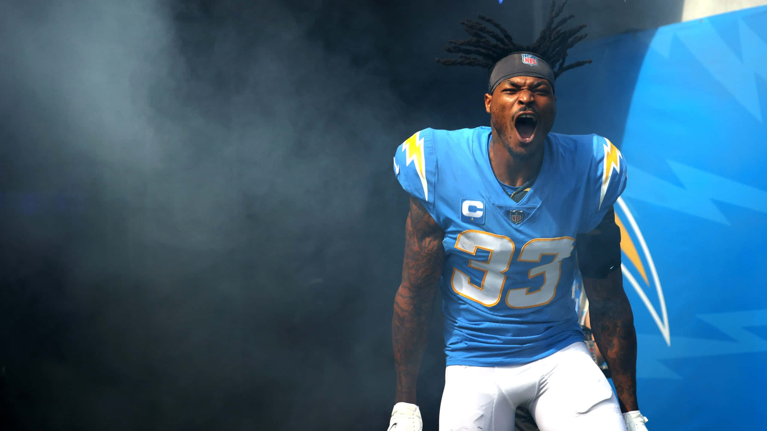 NFL 桌布 壁紙 — 一名身穿藍色球衣、號碼33的美式足球運動員在藍色幾何背景前，穿過煙霧發出勝利的咆哮。