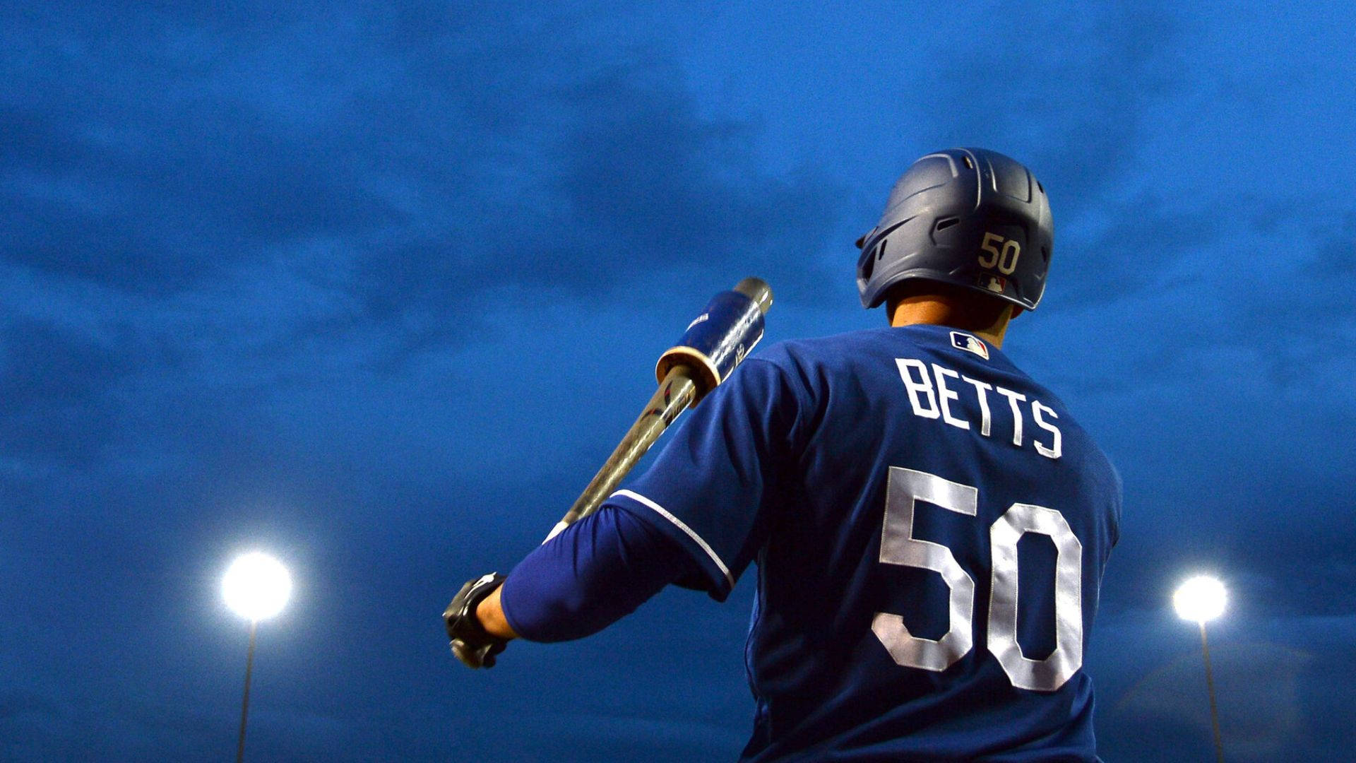 Mookie Betts 桌布 壁紙 — 一名身穿藍色球衣、號碼50、名字BETTS的棒球選手，在夜晚的球場燈光下手持球棒站立。