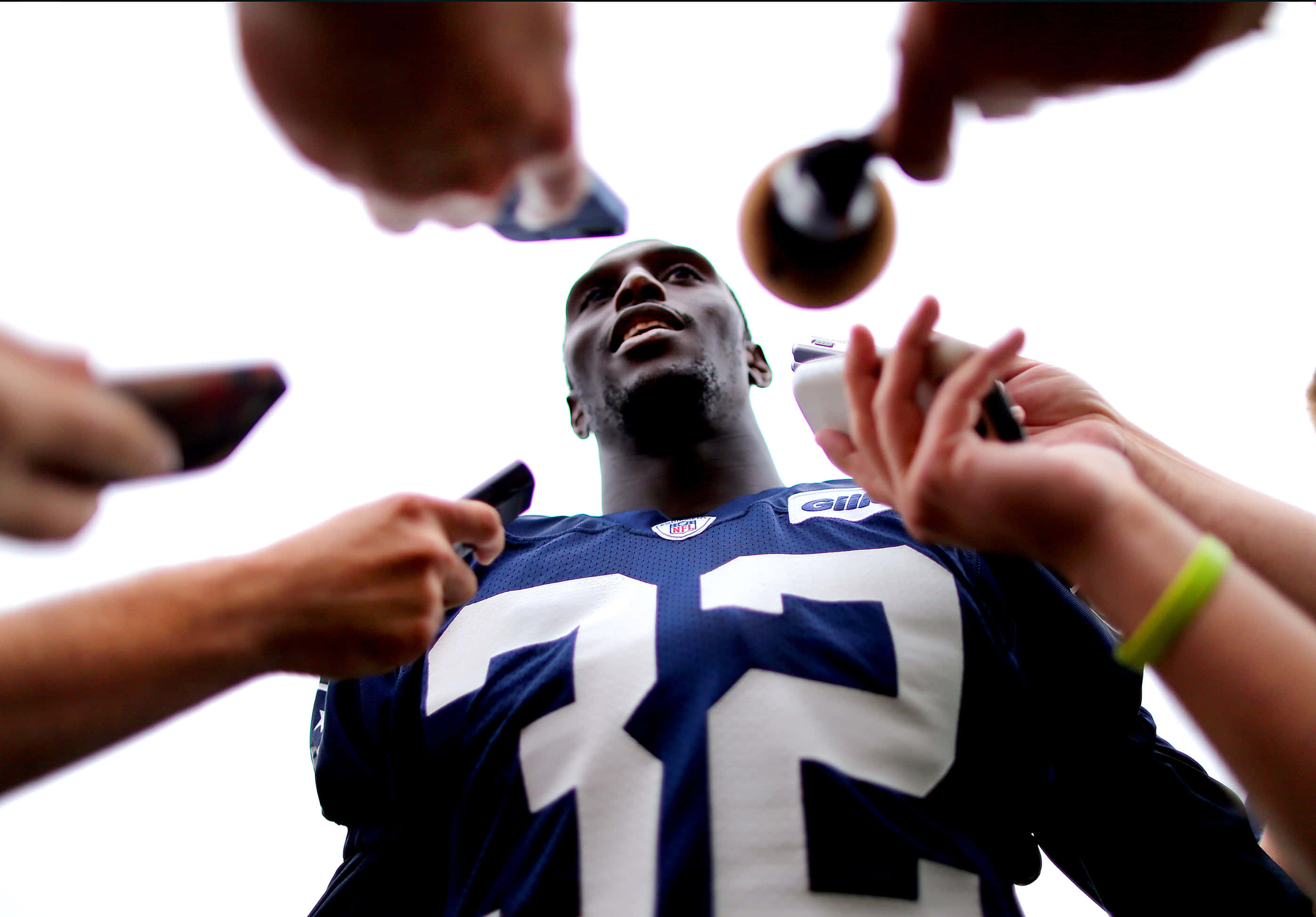 Devin Mccourty 桌布 壁紙 — 一名身穿藍色球衣、號碼72的美式足球員被手持麥克風和電話的記者包圍。