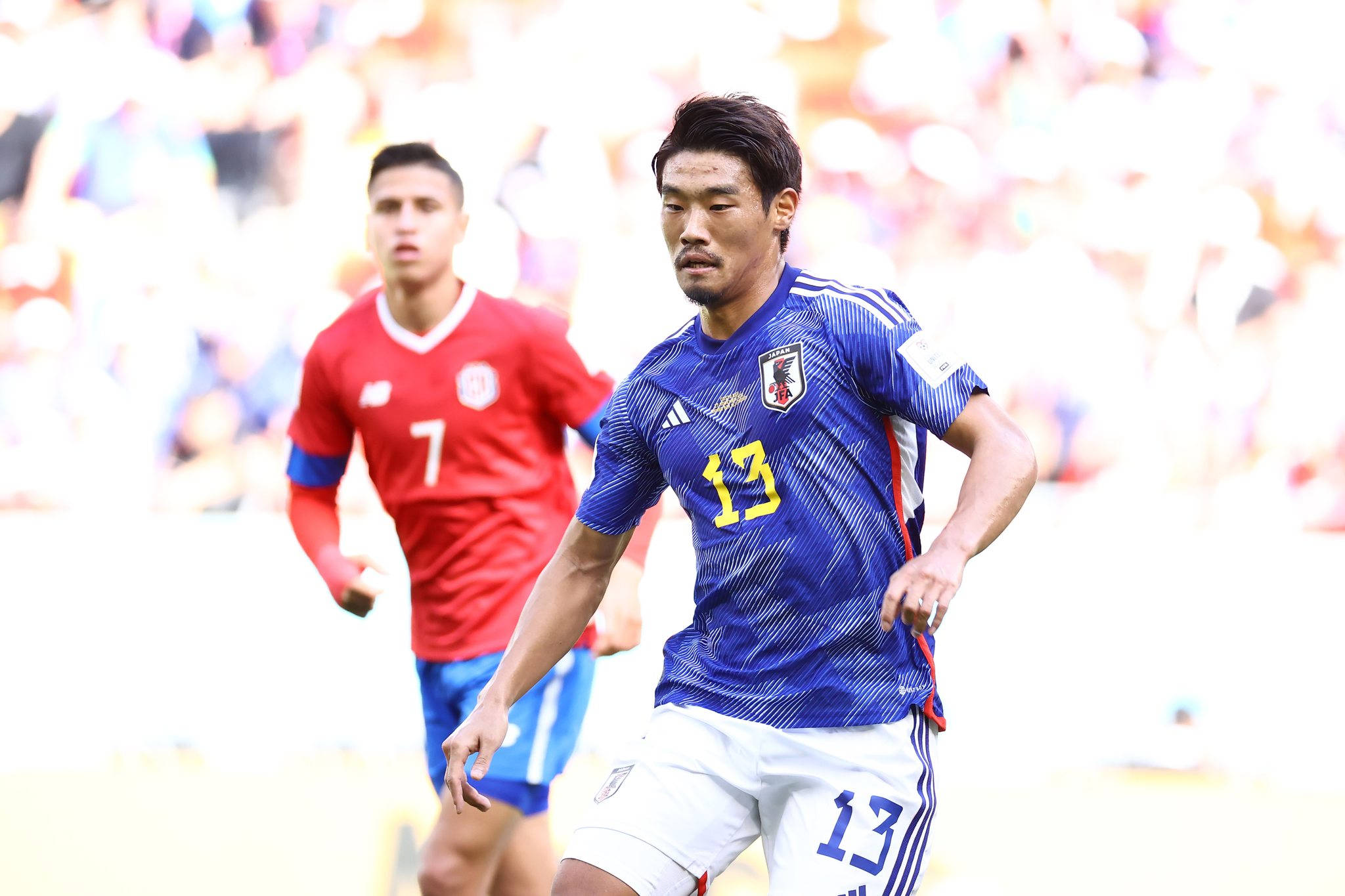 Football Players 桌布 壁紙 — 一名身穿藍色球衣13號的日本足球運動員在日間比賽中激烈奔跑，身後有一個模糊的紅色對手。