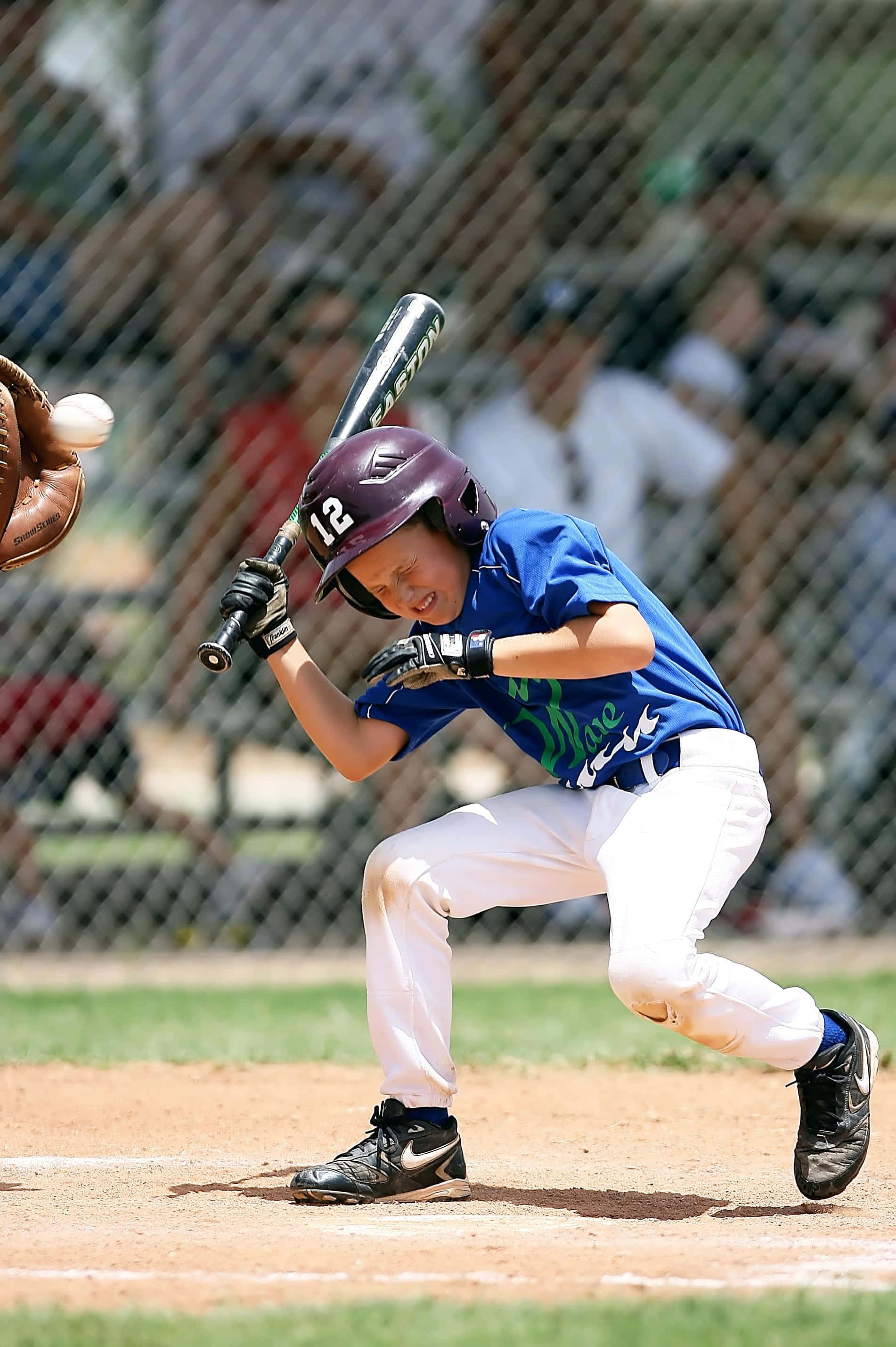 Little League Baseball 桌布 壁紙 — 一名身穿藍色球衣和紫色頭盔的年輕棒球選手，在球接近時，專注地揮動球棒。