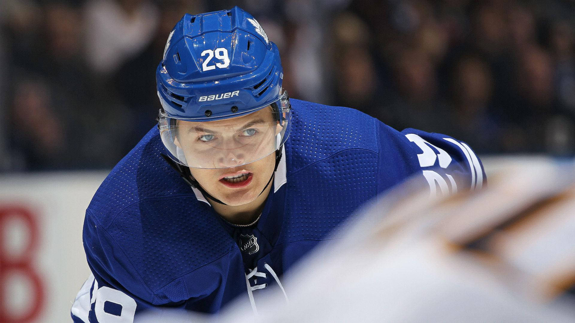 hockey 桌布 壁紙 — 一名身穿藍色球衣和頭盔的專注曲棍球運動員在比賽中激烈前傾，背景是模糊的觀眾。