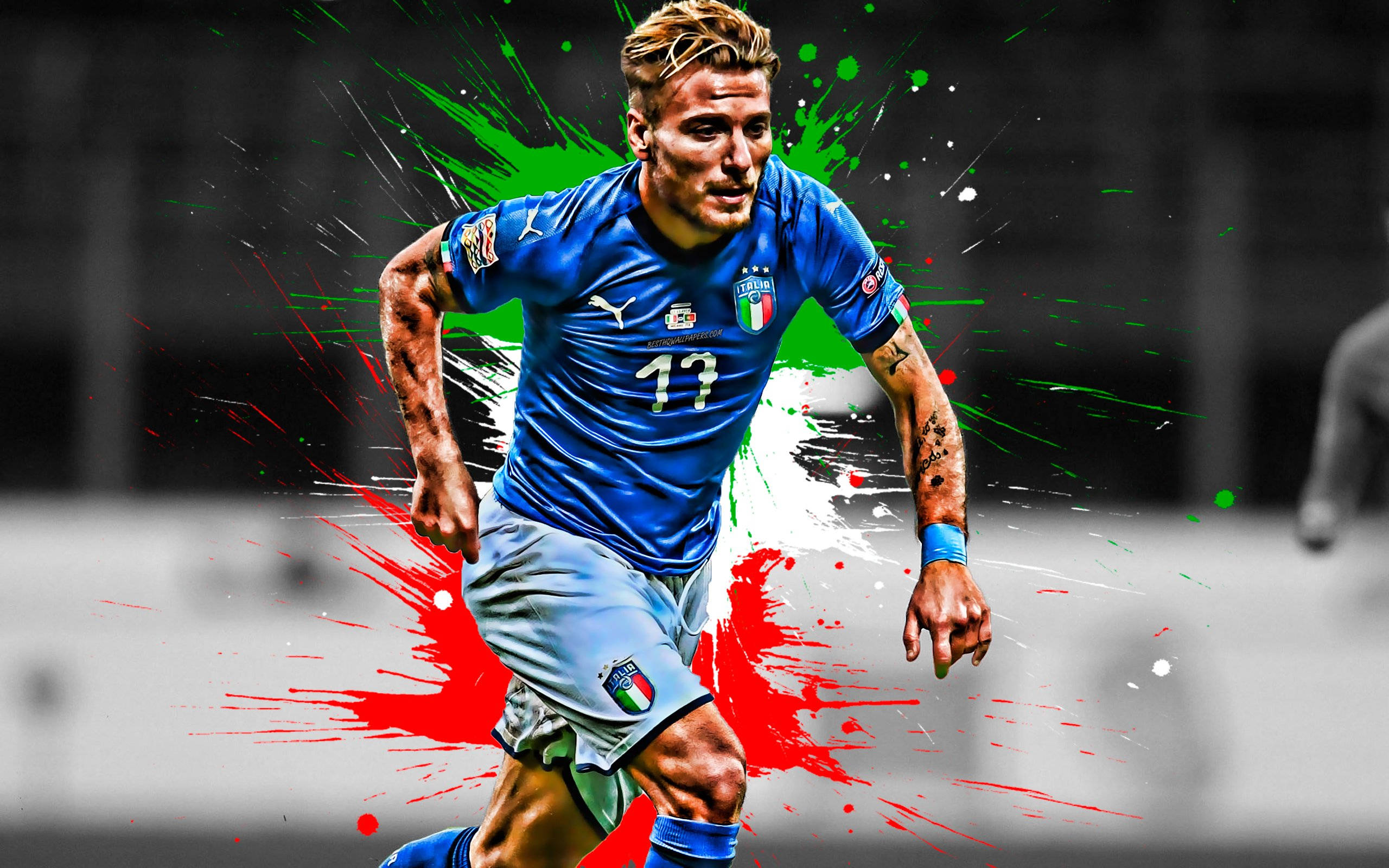 ciro immobile 桌布 壁紙 — 一名身穿藍色球衣的動感足球運動員向前衝刺，周圍爆發出鮮豔的紅色、綠色和白色油漆飛濺。